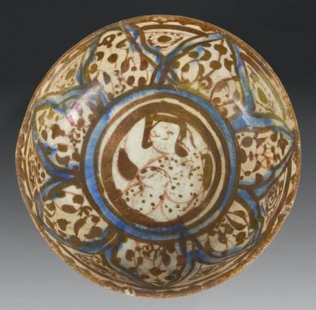Coupe au personnage, Iran, Rey, XIIe siècle Coupe en céramique siliceuse sur petit piédouche à panse carénée, à décor à reflets métalliques et rehauts de cobalt, d'un personnage assis dans un médaillon central, entouré de pétales de lotus. D.: 11,5 cm - H.: 6 cm (Fractures et petits manques)	 Pour une composition similaire dite style monumental, voir O. Watson, Persian Lustre Ware, Londres, 1985, n°17