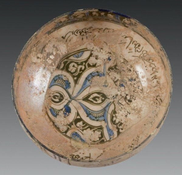 Coupe aux demi-palmettes, Syrie, deuxième moitié du XIIIe siècle Coupe hémisphérique sur piédouche en céramique siliceuse, à décor peint en cobalt et noir sous glaçure transparente sur fond crème. Composition de demi-palmettes dans un médaillon central, bordé par une frise calligraphiée naskhî. Au rebord, frise pseudo-coufique en réserve sur fond noir et rehauts bleus. Au revers, frise épigraphique naskhî et rinceaux foliés. D.: 20 cm - H.: 17 cm (Irisations, fractures recollées, et un petit manque au rebord)