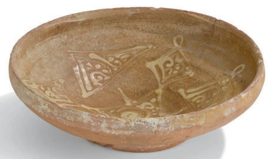 Grande coupe au décor étoilé, Byzance, fin XIIe-XIIIe siècle Coupe à haut rebord, de forme bacino, en céramique argileuse à décor engobé sous glaçure plombifère d'un motif étoilé et pendentifs pseudo -calligraphiques. D.: 28 cm - H.: 8,5 cm (Traces de concrétions, une fêlure) Publication: reproduite dans J. Soustiel, La Céramique islamique, Fribourg, 1985, n°174 p. 149