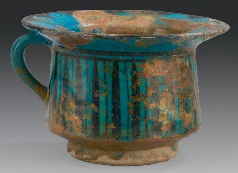 Vase de nécessité, Syrie, Rakka, XIIe-XIIIe siècle Céramique siliceuse à parois verticales sur base annulaire, à large bord. Décor peint en noir sous glaçure turquoise de bandes verticales sur la panse et festons au rebord. D.: 17,5 cm - H.: 11,5 cm (Forte irisation, factures recollées et petits manques)	 	 Cette céramique, décorée selon la technique caractéristique de Rakka aux XIIe et XIIIe siècle, était vraisemblablement destinée à être disposée sous un berceau aménagé à cet effet. Il s'agit d'une pièce rare, dont on ne connaît que peu d'équivalent dans le monde musulman, dont un présenté dans les nouvelles salles du Musée de la Céramique de Sèvres (don J. Soustiel, inv. M.N.C. 21946). Voir sur leur utilisation: J. Mouliérac, «Céramiques et mortier de Samarcande des Xe-XIIe siècles»; Revue d'Histoire de la Pharmacie, n°295, t. XXXIX, 4e trimestre 1992, p. 450, fig. 4. Leur usage était attesté jusqu'à une période récente en Asie centrale, comme en témoigne le récit du voyage d'Ella Maillard, Des monts célestes aux sables rouges, Paris, 1991, p. 240: «Le petit est souriant, sanglé sur sa couche; le berceau est en bois sculpté et sur la grande barre de bois qui le domine reposent deux lourdes couvertures piquées écartées comme un rideau... sous le derrière du gosse; le matelas et le fond de bois sont percés d'un trou régulier sous lequel se trouve un pot de grès garni de cendres.»