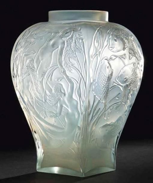 Maison LALIQUE d'après un modèle de Marie- Claude LALIQUE (1935-2003)
Hommage Opale, édition limitée à 999 exemplaires numérotées, modèle créé en 1995 Haut vase en balustre nervurée et à col annulaire. Épreuve en cristal soufflé moulé, en partie satiné. Rendant un hommage appuyé à René LALIQUE en évoquant ses créations, le décor de cette oeuvre se compose de quatre tableaux, un sur chacune des faces: le monde aquatique et ses naïades, le monde sous-marin et ses poissons aux écailles finement ciselées, le monde végétal et ses pinsons blottis dans une ramure de fleurs de pommier et enfin la féminité à travers ces corps alanguis de femmes-fleurs parmi des branchages. Vendu dans son luxueux coffret LALIQUE d'origine. Signé LALIQUE © France sur la base. Hauteur: 30 cm