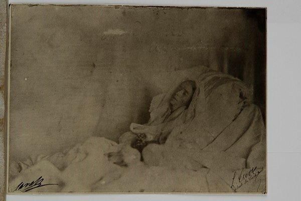 [RACHEL (1821-1858)]. Photographie (contretype ancien) de Rachel sur son lit de mort ; 16 x 21,5 cm.Rarissime photographie de Rachel sur son lit de mort par L. Crette, photographe du Roi de Sardaigne, prise le 4 janvier 1858, le lendemain de son décès au Cannet, avant la mise en bière. Cette photographie, saisissante de réalisme, montrant les traits émaciés de l’actrice, sur laquelle on peut lire la signature du photographe et celle de Sarah Félix, sœur de la tragédienne, a servi de modèle au fameux dessin, très idéalisé et adouci, de Frédérique O’Connell, largement diffusé par la presse et en héliogravure, qui donna lieu à un procès fondateur du droit à l’image.