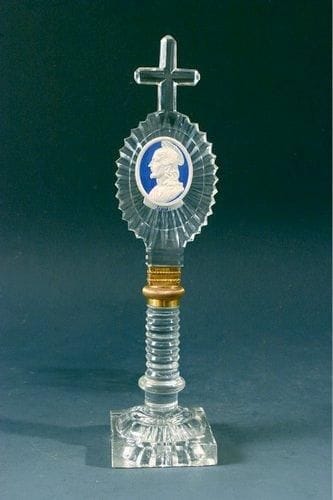 BACCARAT
Ornement sur pied et croix sommitale en cristal taillé de motif rayonnant et cordons, orné d?une médaille représentant le profil de Jésus sur fond bleu; bague intermédiaire en cuivre doré. Haut. 23 cm.