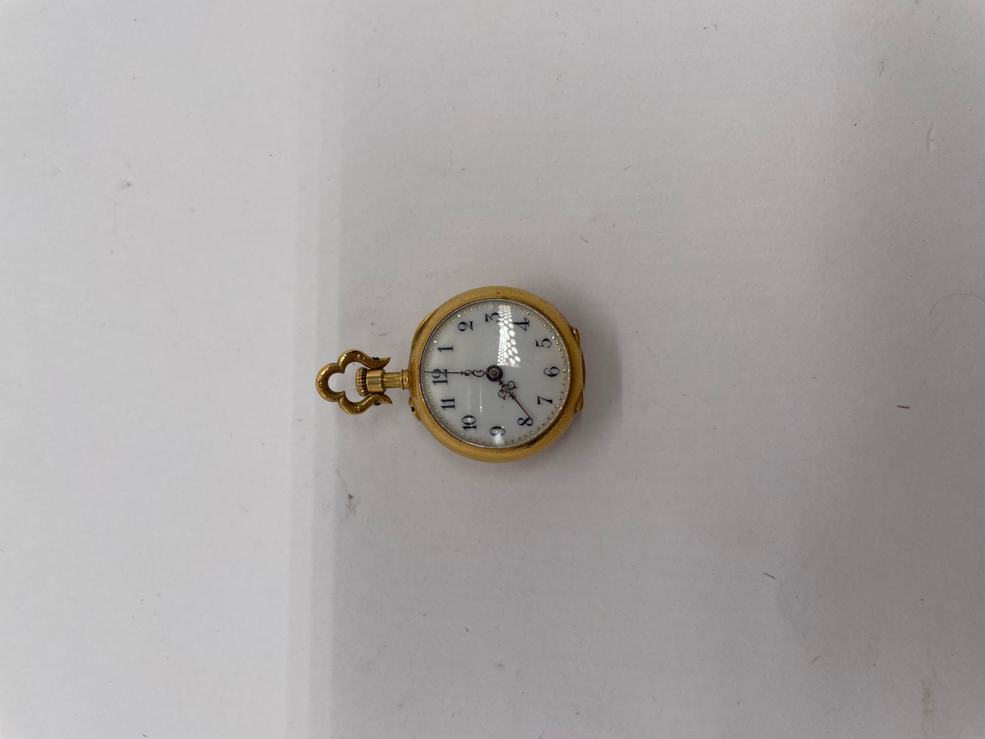 Montre de col en or 750/°°° (18k), le fond à décor de fleurs serties de pierres rouges. 
Double fond en or 750/°°°
Poids brut : 19,6 g