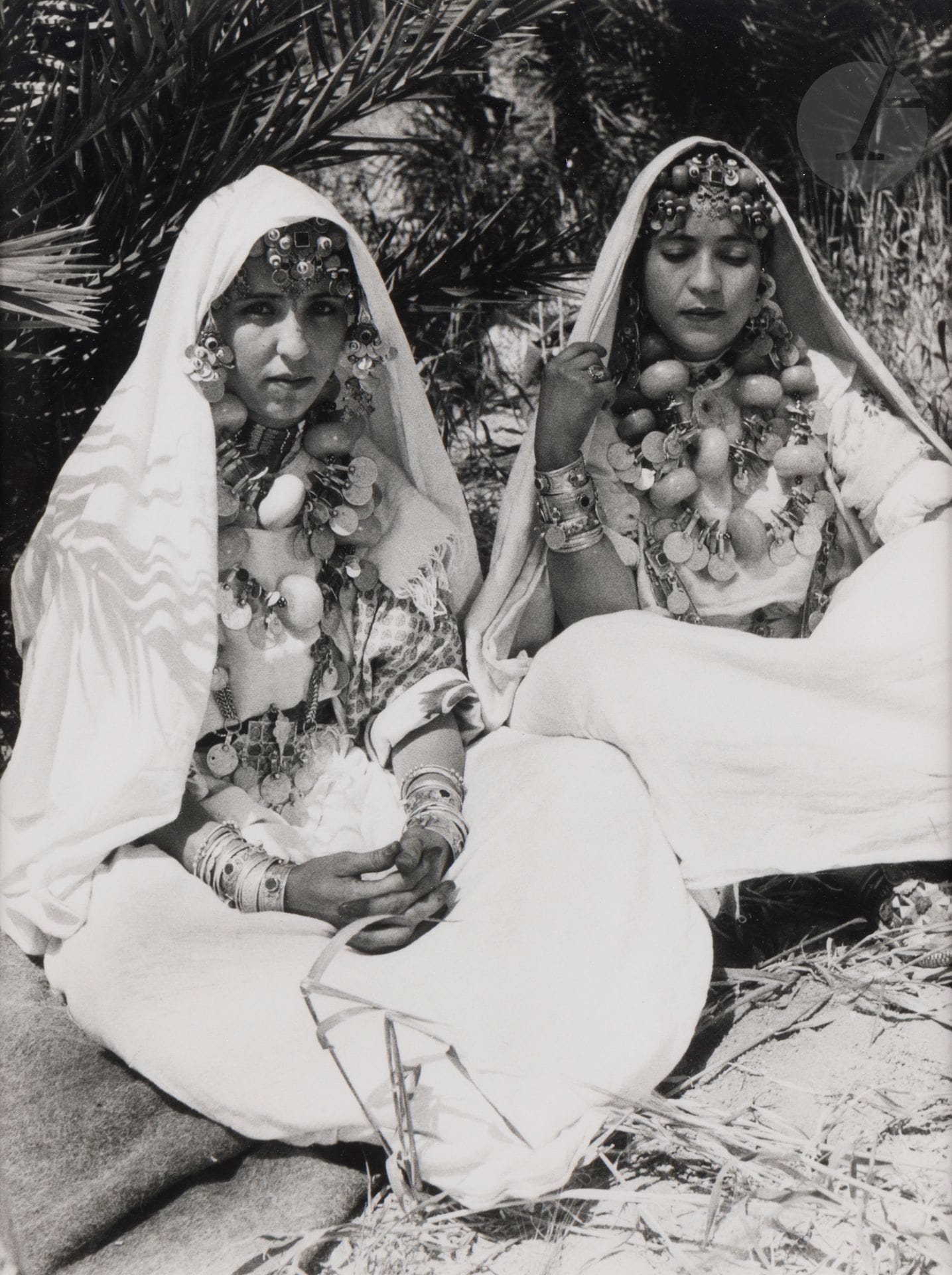 Jean Besancenot (1902-1992) 
Maroc, 1934-1939. 
Anti-Atlas Sud. Tamanait - Costume d’apparat d’une femme de chef berbère. Extrême-sud occidental, Oasis de Tarjicht - La tenue du costume de fête en blanc. Tiznit, Extrême-sud occidental - Trois femmes Chleuh de la corporation des Chikhates musiciennes et danseuses - Voile enlevé, on voit le détail des talgamout, bijoux de tête à chainettes représentant le caractère typique des Ida ou Semlal. Extrême-sud occidental - Oasis Le Tarjicht - Le drapé blanc remplace la cotonnade bleue pour le costume de fête. Extrême Sud occidental - A Tiznit, deux femmes juives dans leur costume journalier - À noter qu’elles portent leurs collier et coiffe de fils d’argent traditionnelle, le « madhour ». 
Cinq (5) épreuves argentiques (c. 1980), montées sous passe-partout, signées au crayon sur les montages en bas à droite. Légendes manuscrites et numéros de négatif au crayon à l’intérieur des montages en bas. 
Format moyen : 24 x 18 cm