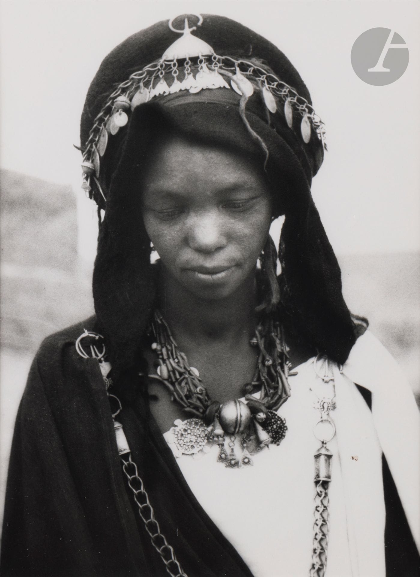 Jean Besancenot (1902-1992) 
Morocco, 1934-1939. 
Central High Atlas. Hartania of the Aït Ounir - Aït Atta group, Aït Atta headdress. Two Aït Isfoul women from the Aït Atta group - they are dressed in blue cotton garments, the veil enveloping a curious headdress armed with a large leather ring. Berber woman from the Aït Atta group, veil parted, revealing the effect of the blue and white drapes stapled together by the chain fibulas. 
Three (3) silver prints (c. 1980), matted, signed in pencil on the mounts lower right. Handwritten captions and negative numbers in pencil inside the mounts below. 
Medium format: 24 x 18 cm