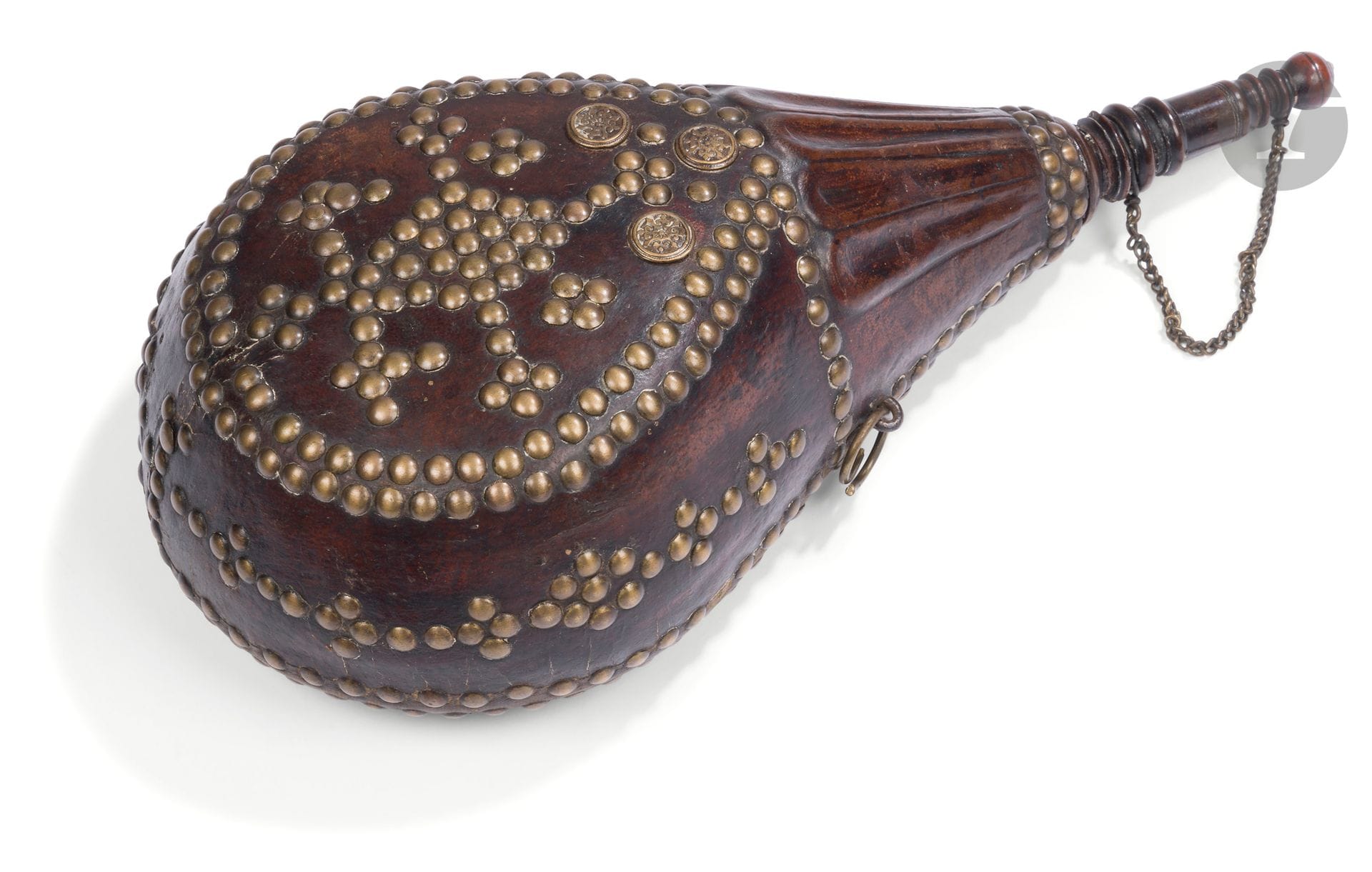 Berber powder flask known as rbi'a del baroud, Morocco, Middle Atlas, late 19th - early 20th century 
A leather pear-shaped powder flask on a wooden core, topped by a cylindrical turned-wood mouthpiece closed by a turned-wood stopper with a bone end to which it is attached by a chain. The entire body is adorned with brass nails in several lines, diamond-shaped and cruciform motifs, complemented by three metal medallions with rosette decoration. The leather on the upper part is embossed to form tongues, and two metal rings on the sides allow a hanging cord to be attached. 
Height: 36 cm; max. width: 17 cm 
Small loss at the end of the stopper, cracks, small losses in the back leather.