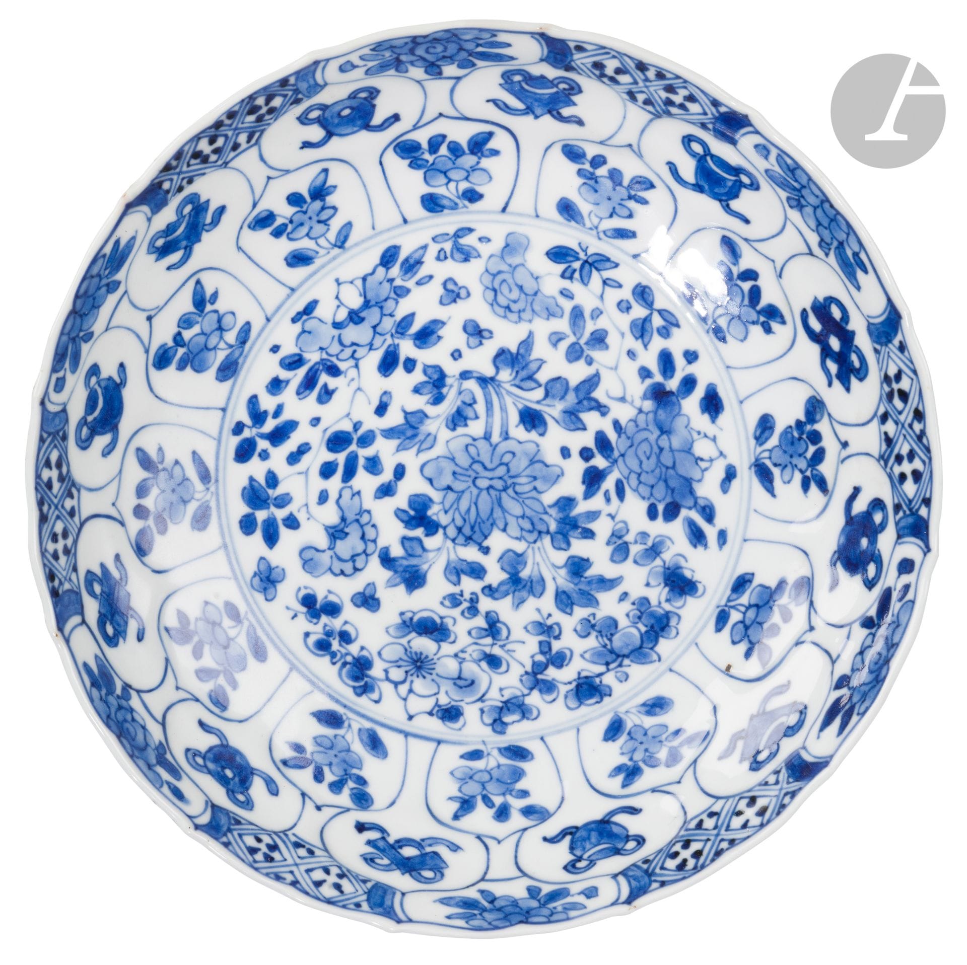 Deux assiettes en porcelaine bleu et blanc, Chine, époque Kangxi (1662-1722) 
De forme lobée avec des bords en accolades, chacune à décor central de fleurs de pivoines ou prunus avec leur feuillage. Les marlis sont ornés de petits panneaux rayonnants en forme de pétale et renfermant des décors de fleur, objet précieux ou motif stylisé. L’extérieur des assiettes montre le même décor. Marque à six caractères 苛 玉宝鼎之珍 - qi yu bao ding zhi zhen en bleu sous couverte dans un double cercle bleu à la base.
Diamètre : 22 cm