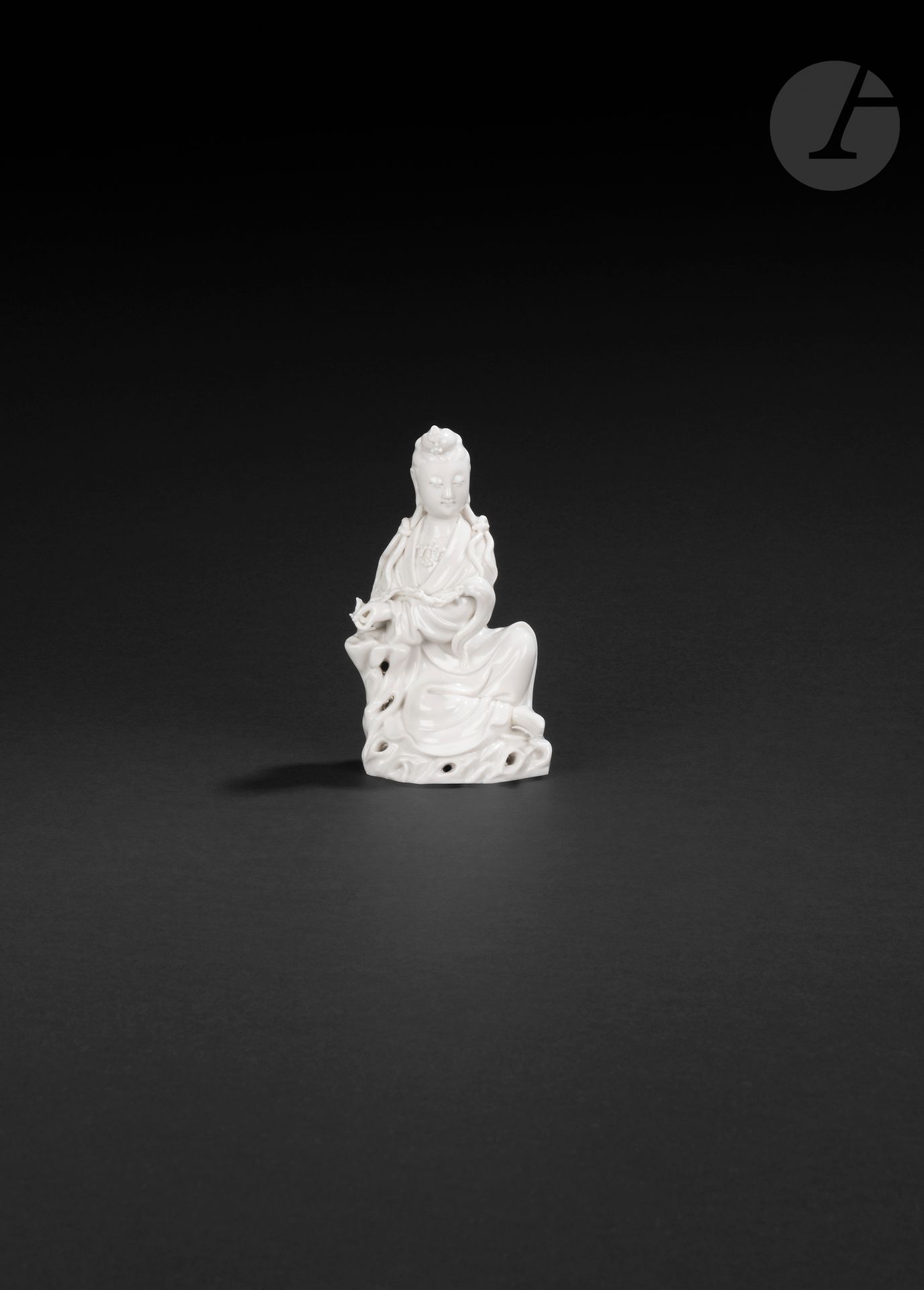 Small Chinese white porcelain guanyin, China, Dehua, 19th - 20th century
She is depicted seated on a pierced rock, wearing a long pleated robe and a pearl necklace. Her serene face features a slight smile, the forehead is adorned with the urna and the earlobes are elongated. The hair is gathered into a small bun, adorned at the front with an ornament, and divided at the back into two long locks passing over the front of the shoulders and knotted to form two new locks. His left arm rests on a rock and his hand holds a fuzi. The naked right foot protrudes from the bottom of the dress. On the back is a molded double-gourd mark, difficult to identify.
Height: 13.5 cm
Foot and top of headdress ornament reattached.