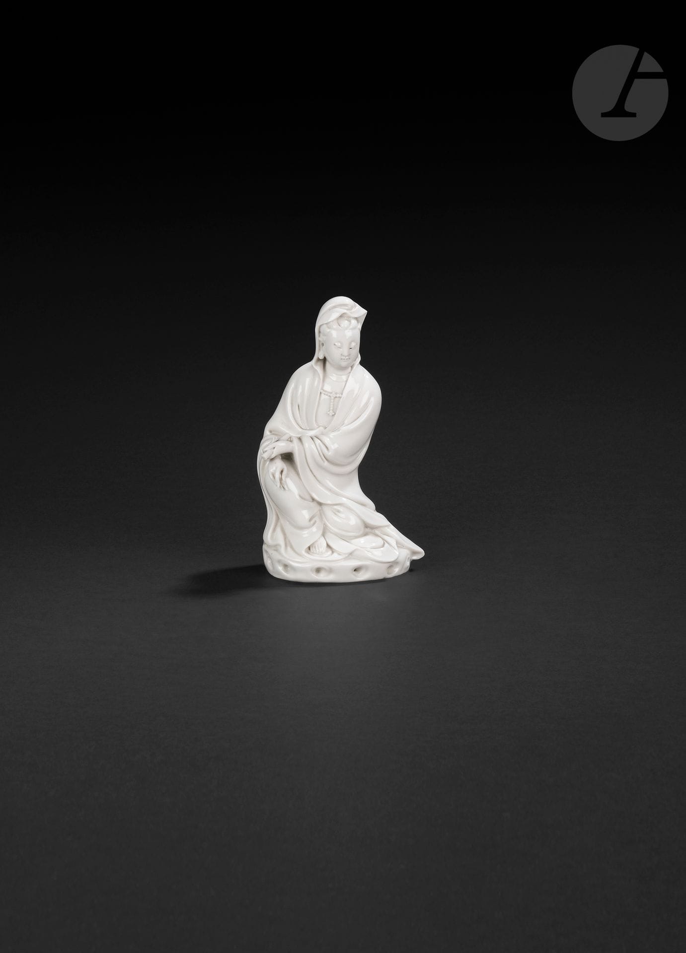 Guanyin in Chinese white porcelain, China, Dehua, 17th - 18th century
Depicted seated on a small base depicting rocks, wearing a long pleated robe open to the chest and adorned with a pearl necklace. Her face is serene, her eyes downcast and her hair covered by the robe. Her forehead is adorned with a central urna, and her earlobes are elongated. She holds a scroll in her left hand. Her bare right foot protrudes from the bottom of her dress. On the back is a molded double-gourd mark, difficult to identify.
Height: 15.5 cm
A broken finger on the left hand.

Provenance: 
E&amp;J Frankel Collection" label.