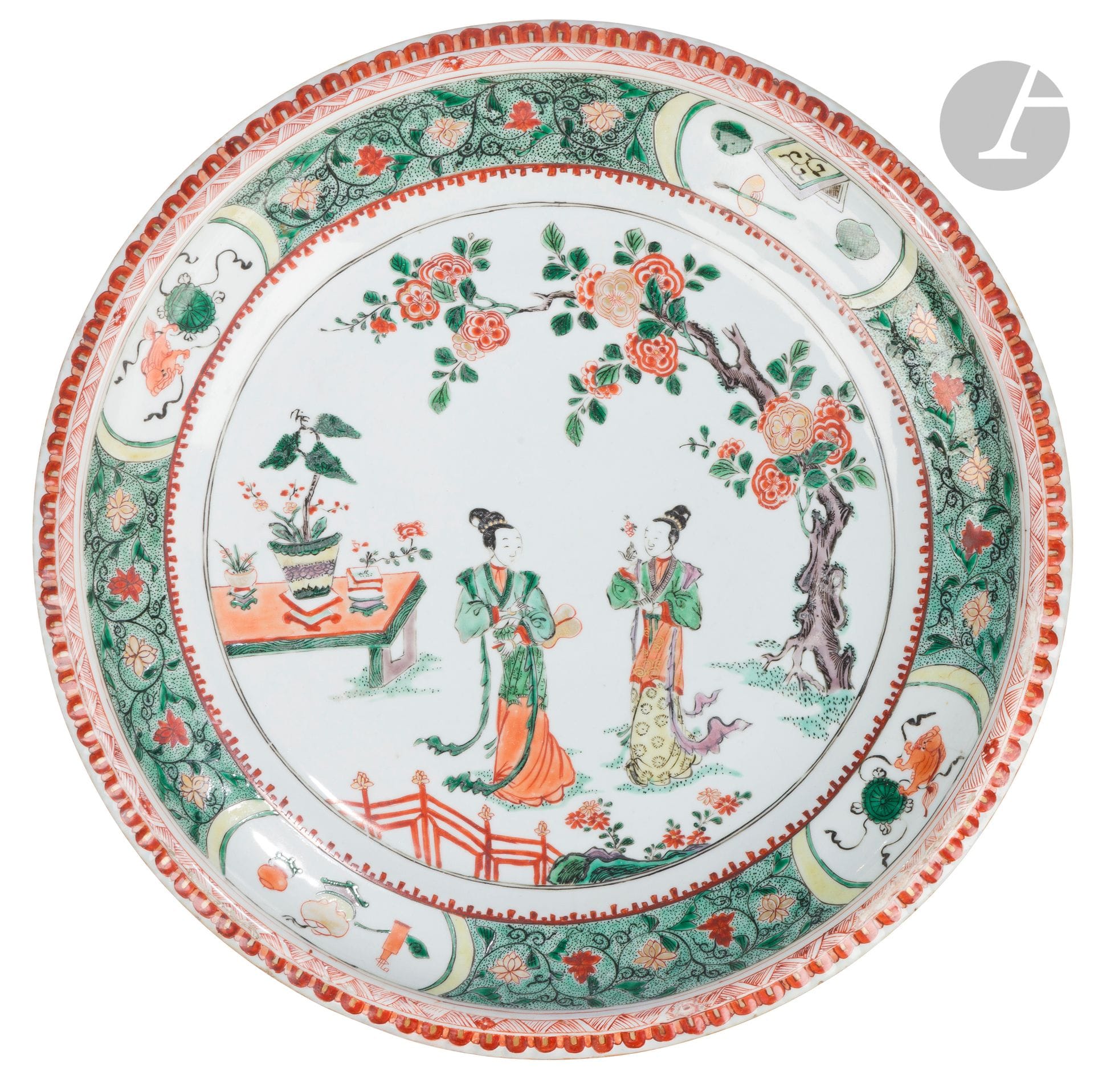 Large porcelain dish in green family enamels, China, Kangxi period (1662-1722)
Godronné rim, with central decoration of two women, one holding an osmanthus flower, the other a fan. They are standing next to a flowering tree and a garden table with planters. The marli is adorned with scrolls of lotus flowers and alternating medallions showing a Fô dog playing with a brocade ball and household objects. On the reverse, four branches of peonies and a double blue circle.
Diameter: 38 cm
Restoration to edge, fels.