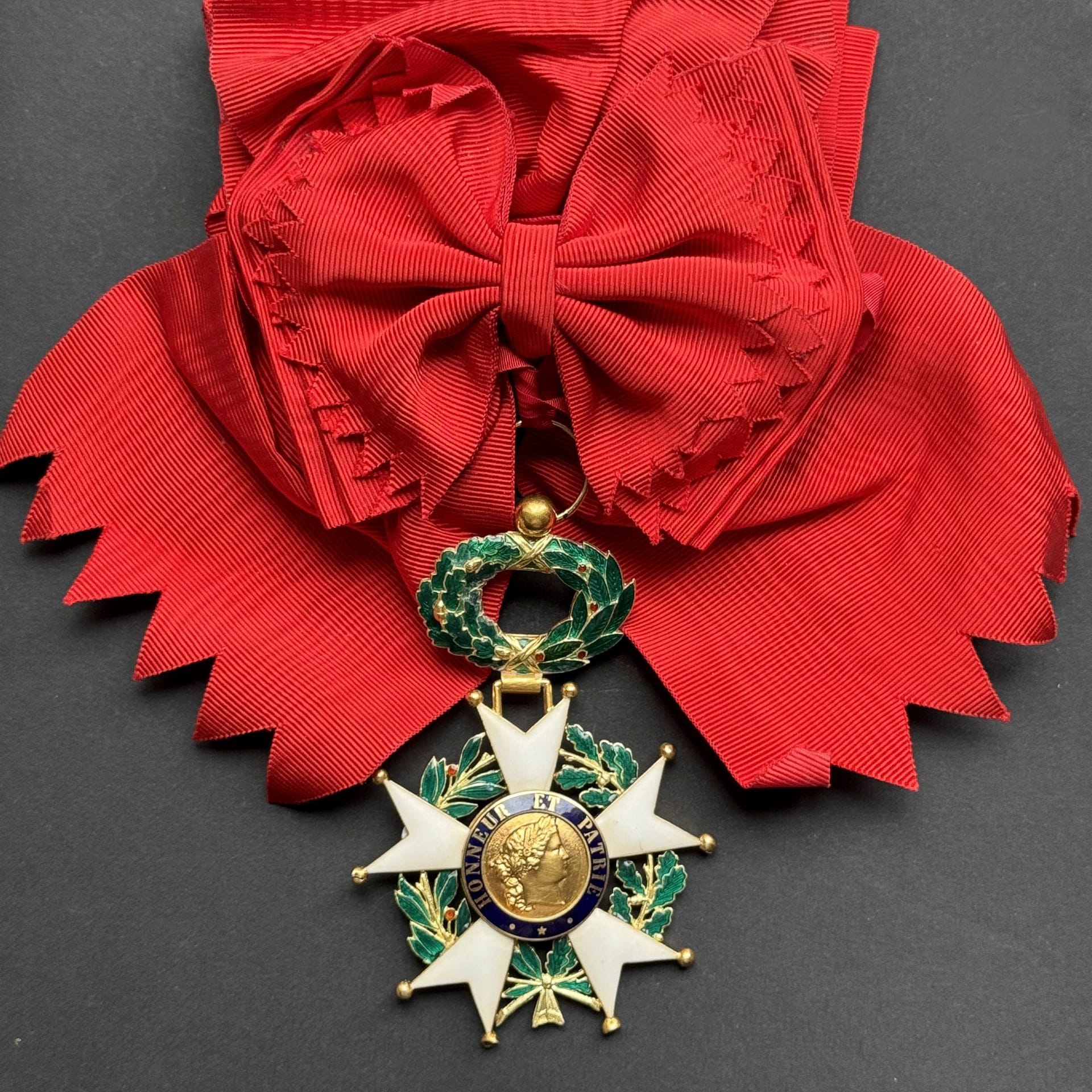 FRANCE 
ORDRE DE LA LÉGION D’HONNEUR 
Bijou de grand-croix d’époque IIIe République. 
En or et émail (accident à deux boules, éclat à un drapeau). Branches émaillées blanches mat à froid (probablement postérieurement). 
Centre à légende d’avers « HONNEUR ET PATRIE » et revers « REPUBLIQUE FRANCAISE 1870 ». 
Poinçon tête d’aigle sur la pampille. 
100 x 66 mm - Poids brut : 50 g
On y joint une écharpe de grand-croix de fabrication moderne. 
B.