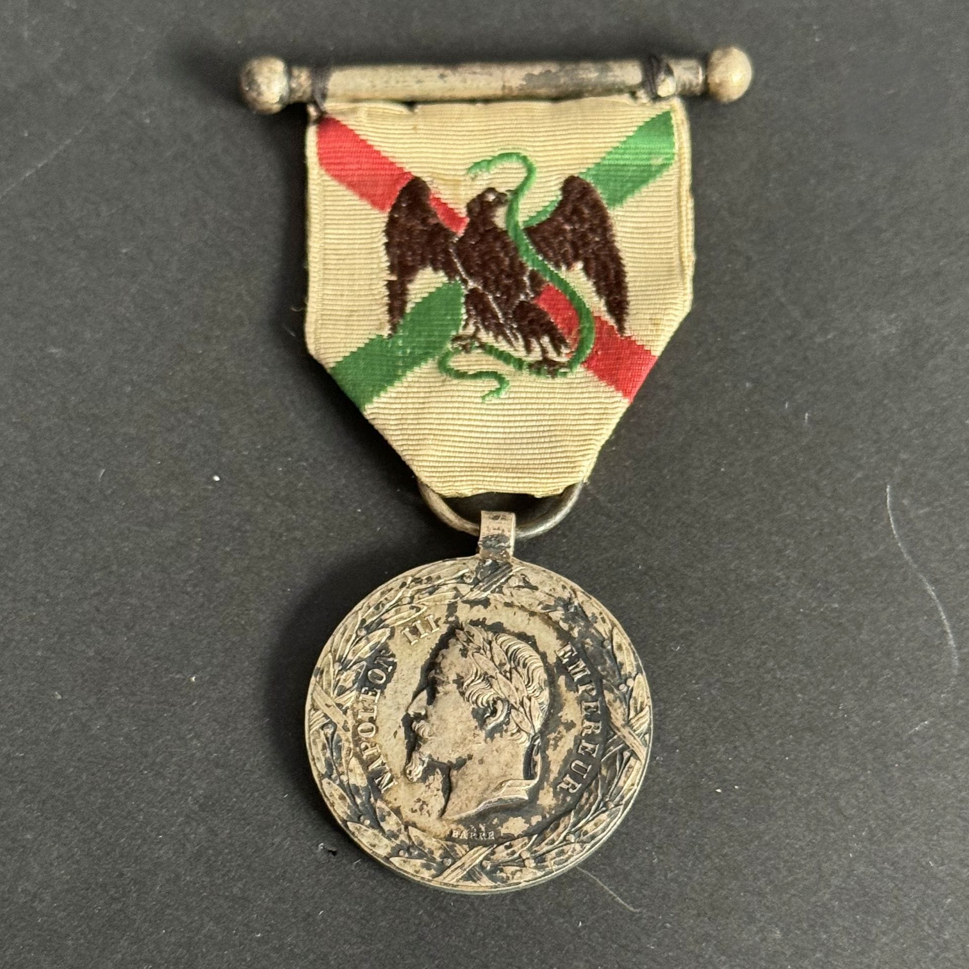 FRANCE 
MÉDAILLE DE LA CAMPAGNE DU MEXIQUE (1863)
Médaille de l’Expédition du Mexique (1862-1863), par BARRE. 
En argent (oxydé). Ruban à l’aigle avec barrette cousue. Poinçon rectangulaire tête d’aigle.
29 mm - Poids net : 14 g 
T.T.B.