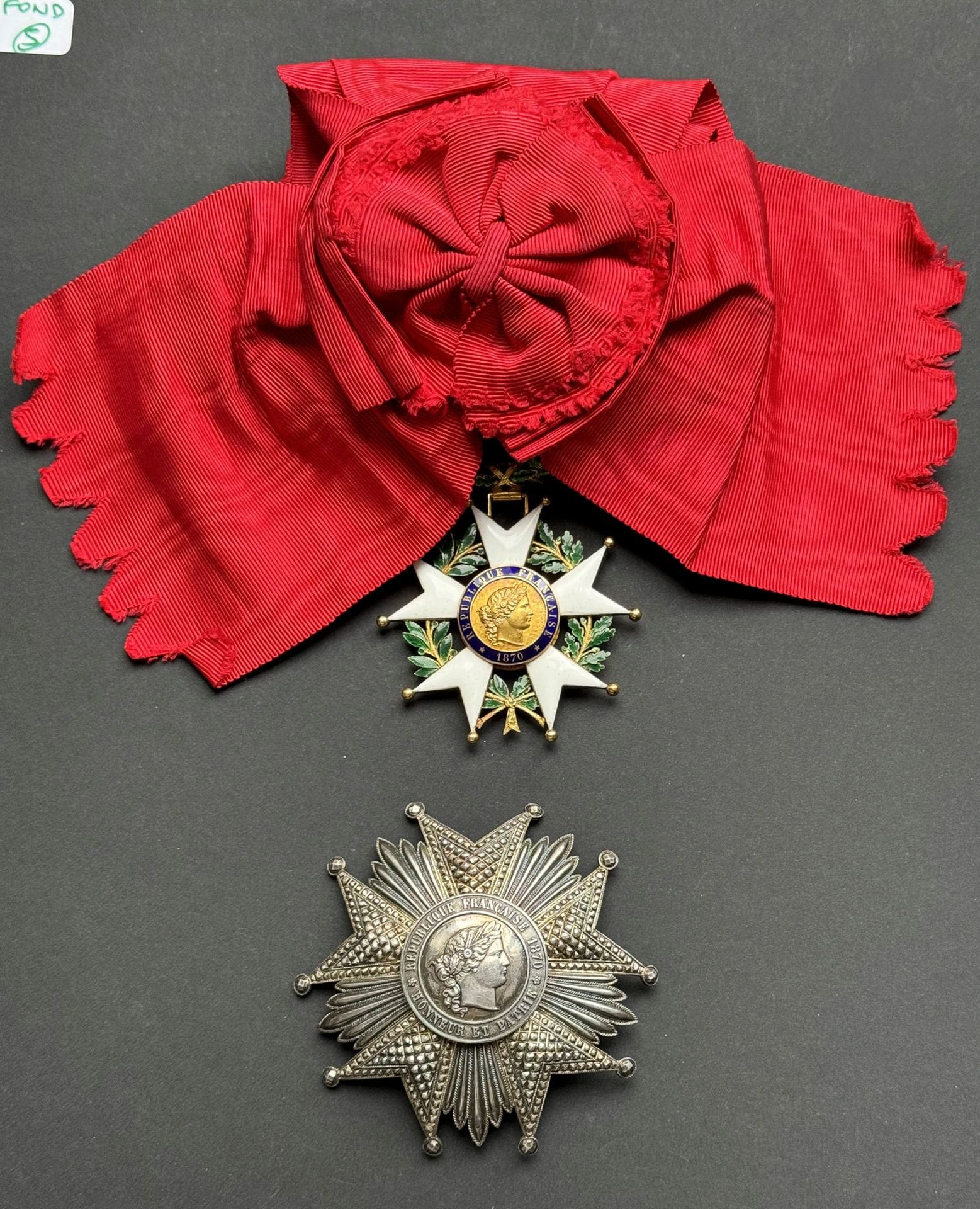 FRANCE 
ORDRE DE LA LÉGION D’HONNEUR 
Ensemble de grand-croix d’époque IIIe République de fabrication Ouizille Lemoine comprenant : 
- Plaque.
En argent, travaillé en pointes de diamant, le centre en trois parties. 
Revers à attache basculante et deux crochets, avec marque du fabricant « OUIZILLE LEMOINE LEMOINE FILS SUCeur JOAILLIER DE LA LÉGION D’HONNEUR RUE St HONORE 356 PARIS » 
Poinçon tête de sanglier et d’orfèvre Victor Lemoine. 
Poids : 88 g
- Bijou.
En or et émail. Poinçon tête d’aigle et d’orfèvre V.L (Victor Lemoine) sur l’anneau. 
100 x 68 mm - Poids brut : 63 g
Avec écharpe d’origine en moire, avec nœud. 
T.T.B. à SUP.