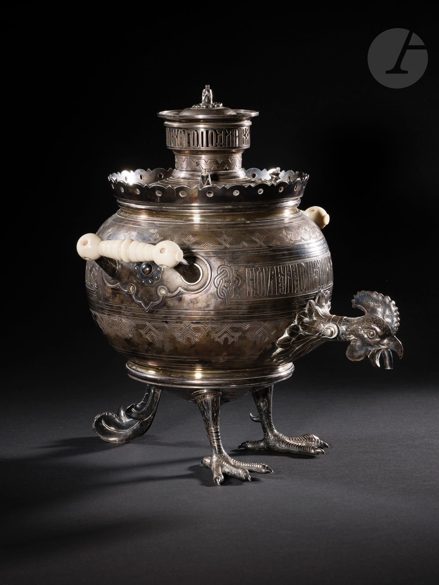 Firme des successeurs de Pavel Ignatievitch SAZIKOV. Moscou, 1882.
Important samovar « coq » en argent, modèle dessiné par Ippolit Antonovitch Monighetti.
Intérieur en vermeil. Poignées en résine (postérieures). Boutons de préhension absents. La couronne porte un dicton découpé à jour : « ТАКОГО ПОДЛИВАЛО НИГДѢ НЕ БЫВАЛО » (« il n’y a nulle part une telle verseuse ») et le corps un dicton gravé en relief « САМОВАРЪ ЧТО МОРЕ СОЛОВЕЦКОЕ, ПЬЮТЪ ИЗЪ НЕГО ПРО ЗДОРОВЬЕ МОЛОДЕЦКОЕ » (« le samovar est comme la mer de Solovki, on boit de lui à la santé des braves »).
Poinçons : 84, Moscou 1882, essayeur « А·К » (Alexandre Stakhevitch Koudrine) et orfèvre « САЗИКОВА » surmonté de l’aigle de fournisseur à la Cour (fabrique de SAZIKOV).
Hauteur : 32 cm ; poids brut : 3547 g

Le samovar coq est un objet emblématique en Russie : rares sont les collections privées ou publiques qui peuvent s’enorgueillir d’en posséder un exemplaire. 
Les exemplaires connus actuellement sont en tombac ou en laiton. - Deux exemplaires se trouvent au Musée Historique d’État à Moscou. 
- Un au Musée Russe à Saint-Pétersbourg. 
- Un au Musée d’histoire et de traditions locales de Poudozh (Carélie). 
- Le musée privé des Samovar et bouillottes (à Toula) en possède un exemplaire provenant de la collection Lobanov. 
- Deux autres exemplaires sont répertoriés par L. A. Petrova : l’un en Italie et l’autre dans une collection aux États-Unis (photographies non disponibles). 
- Trois autres exemplaires différents sont présentés sur un site du forum de samovar russe. - Un exemplaire a été vendu aux enchères en 2017 (Orne enchères). 
- Un exemplaire en Ukraine. 
Il n’est pas exclu que d’autres exemplaires figurent dans des collections privées. 

La première mention trouvée du samovar coq date de 1869 dans le journal russe « Всемирная Иллюстрация » (« Le monde illustré », t. I, N°14, p. 212) où son dessin est attribué à Ippolit Monighetti, ce qui est confirmé dans le compte-rendu de l’Exposition manufacturière panrusse à Saint-Pétersbourg en 1870 : « Почти во всѣхъ издѣліяхъ г. Морана открывалось важное достоинство оригинальности. Особенное внимапіе обращали на себя царскія врата и люстры въ внзаптійскомъ вкусѣ, также томпаковые самовары и въ чнслѣ ихъ одинъ въ видѣ пѣтуха но рисунку профессора Монигетти » (« Presque dans toute la production de M. Moran [Pierre Adolphe Morand 1818-1900], se révèle une originalité de grand mérite. Une attention particulière ont attiré des portes royales et des lustres dans le goût byzantin ainsi que des samovars en tombac parmi lesquels un exemplaire en forme de coq d’après le dessin du professeur Monighetti »). 

Ippolit Antonovitch Monighetti (1819-1878) était non seulement un architecte officiel de la Cour, mais également un des promoteurs du style russe (ou néo-russe), dans les années 60 et 70 de son siècle, à l’époque où le futur Alexandre III était encore tsarévitch grand-duc héritier Alexandre Alexandrévitch. Ce dernier était viscéralement partisan du tout ce qui était national. Ce n’est donc pas un hasard si le samovar qui se trouve aux États-Unis (cité par L. A. Petrova), daté de 1866, est le premier exemplaire connu de ce type : il porte une inscription « АЛЕКСАНДРЪ АЛЕКСАНДРОВИЧЪ И МАРИЯ ФЕОДОРОВНА  / ДАНИЯ 31 ИЮНЯ 1866 / С. ПЕТЕРБ 28 ОКТ 1866 » (« Alexandre Alexandrovitch et Maria Feodorovna / Danemark 31 juillet 1866 / S. Peterb 28 oct 1866 »; la transcription est donnée non d’après l’original mais d’après la citation de l’article de L. A. Petrova). Cependant, déjà en 1863 un samovar prototype de ce modèle (même forme, mais sur trois pattes de coq et avec un robinet sans la tête de coq) avait été offert par I. Monighetti à un certain A. N. Chestov (actuellement au GIM). 53 Il apparaît souvent dans les descriptions de ce samovar (aussi bien dans les catalogues de musée que dans les divers articles ou forums consacrés au samovar) qu’il a reçu une médaille d’or à l’Exposition universelle de Vienne en 1873. Il n’y a malheureusement aucune confirmation de cette assertion qui de plus semble erronée dans la mesure où à l’Exposition de 1873, il n’y avait pas de médaille d’or mais des médailles du mérite (8687), de progrès (2929), pour les collaborateurs (2162), médailles d’art (977), de bon goût (310), des diplômes de reconnaissance (10166) et des diplômes d’honneur (441). 

FICHE COMPLETE DISPONIBLE DANS LE CATALOGUE PDF.