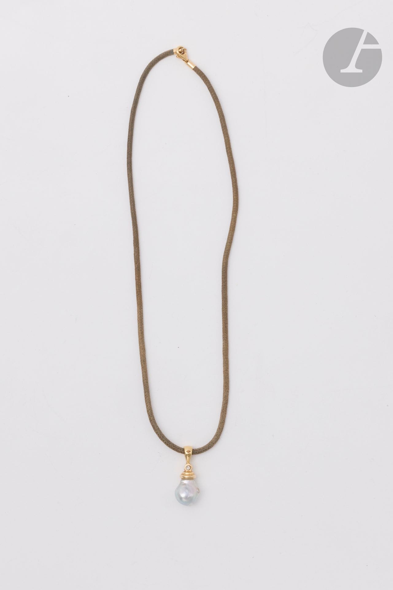 Pendentif en or 18K (750), la bélière agrémentée d'un diamant rond de taille brillant retenant une perle de culture baroque grise, coulissant sur un cordon en coton le fermoir en or 18K. Hauteur pendentif : 2,7 cm environ. Longueur cordon : 40 cm environ. Poids brut : 5,6 g (aspérités de surface)