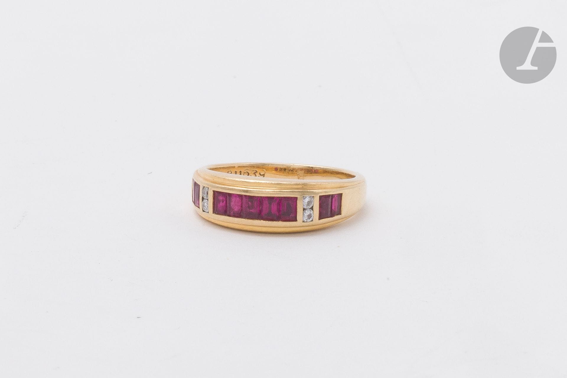 Bague en or 18K (750) sertie d'une ligne de rubis calibrés doublement scandée de diamants ronds de taille brillant. Tour de doigt : 51. Poids brut : 4,9 g (déformation, égrisures)