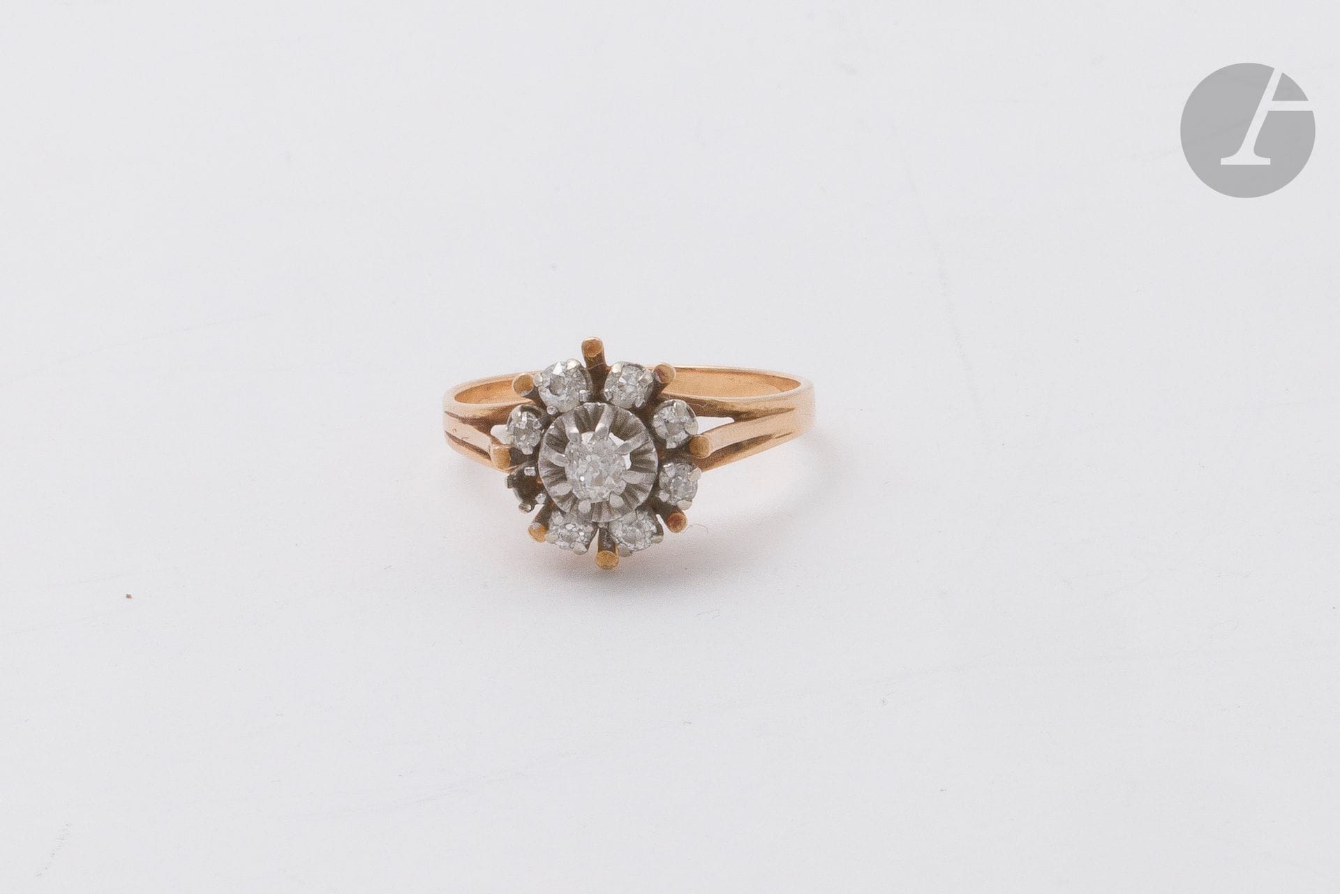 Bague fleur en or 18K (750) et platine, le cœur serti d'un diamant arrondi de taille ancienne, l'entourage piqué de 7 diamants arrondis de taille ancienne plus petits sur platine. Travail français. Tour de doigt : 60. Poids brut : 4,5 g (manque, égrisures)