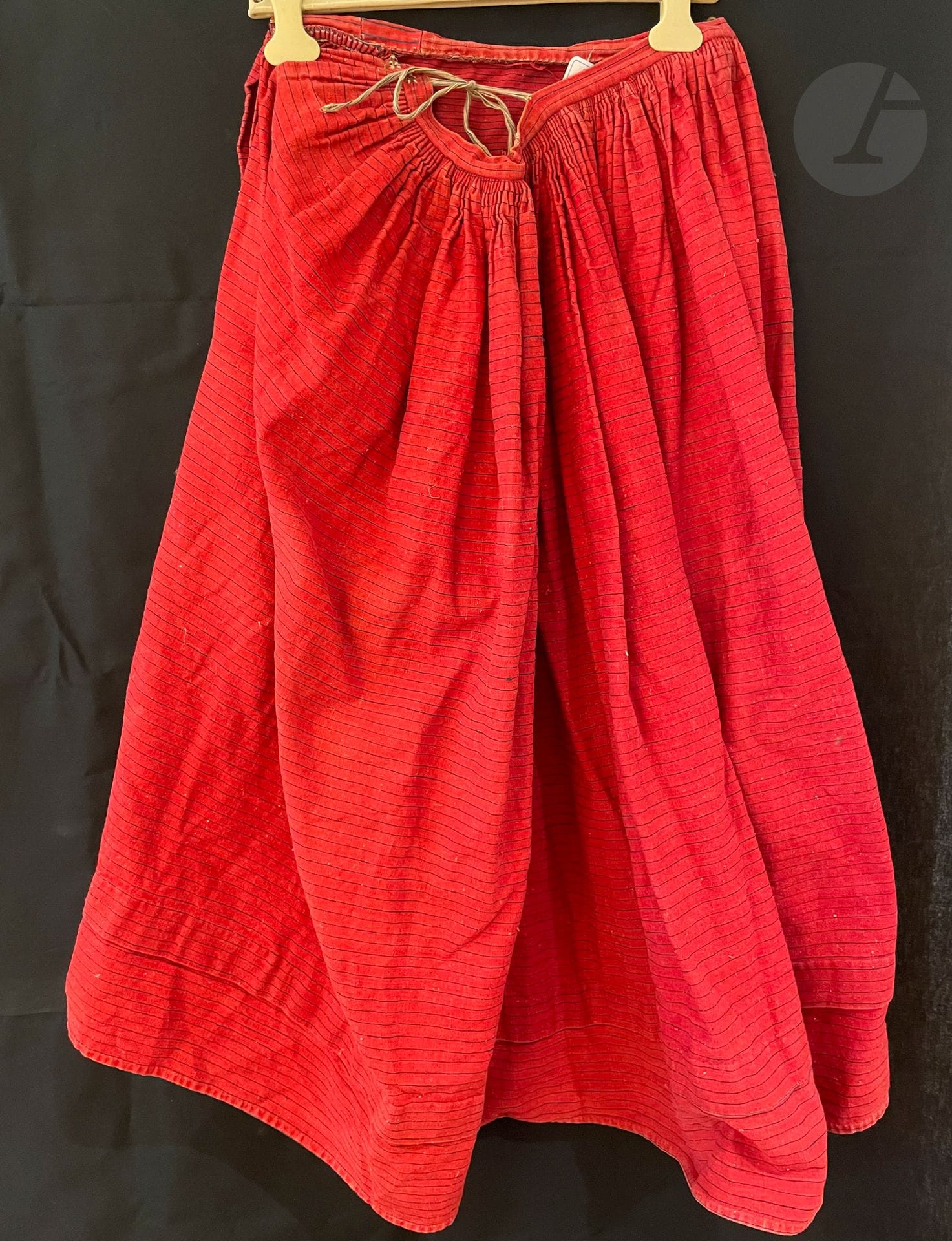 Réunion d'une jupe paysanne en siamoise teint à la garance et jupon de bal en piqué blanc, Alsace, XIXe siècle. La jupe rouge barrée d'un filet indigo montée à plis canons sur bande de taille (très bel état) H : 92 cm et un jupon en piqué blanc à ourlet festonné.