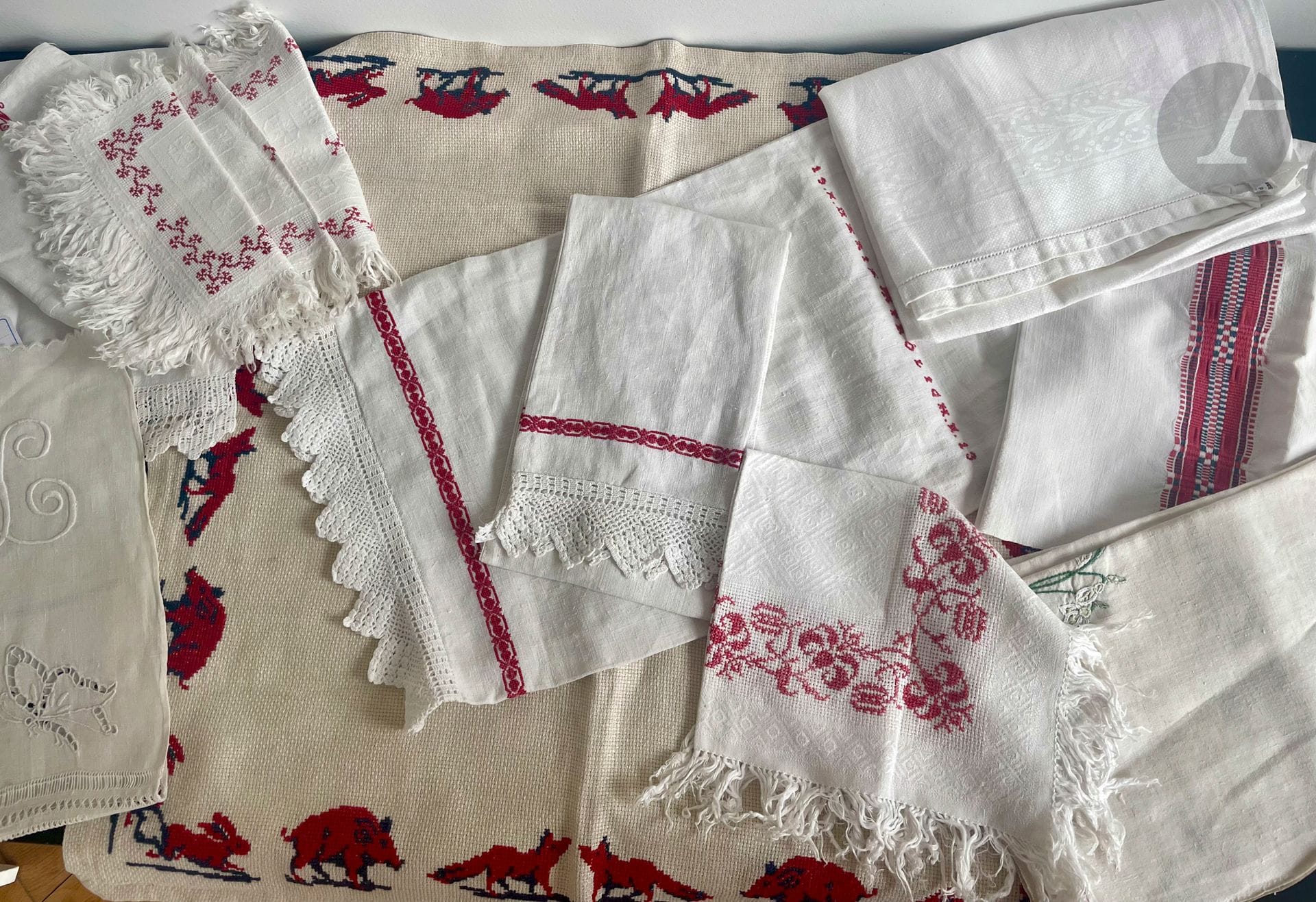 Une quinzaine de pièces de trousseau bourgeois en damas de lin brodé et orné de dentelle au crochet, Alsace, fin XIXe -début XXe siècle dont : un tapis de jeux ou petite nappe brodée d'animaux de la chasse au point de croix en laine ; une pochette et un sac brodé " Maria Froligh 1913 ", 5 belles serviettes en damas de lin à franges et fils tirés, rebrodés au point de croix en rouge, nappe ou torchon à liteau façonné en damiers en rouge et bleu, torchons en lin épais rebrodés de fleurs ou cœurs au point de tige.
