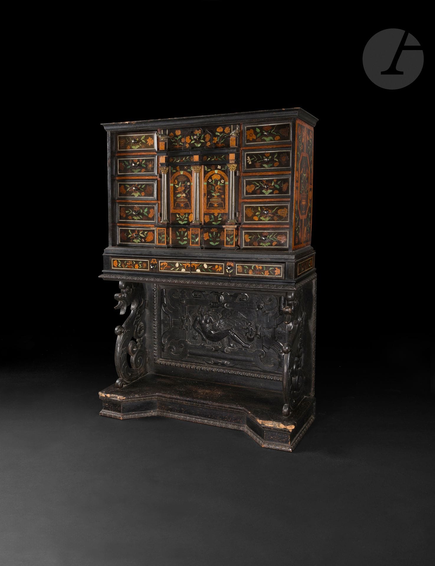 Cabinet en marqueterie de fleurs, en bois et ivoire teintés, ouvrant à quinze tiroirs et deux vantaux découvrant un intérieur à neuf tiroirs, parquet à damier et miroirs en perspective, reposant sur un piétement (partiellement refait) en ébène et bois noirci à décor de Léda et le cygne, les montants à figures de dragon (rapportées à une date ultérieure); (accidents et manques).
Milieu du XVIIe siècle, vers 1660.
H. 179cm, L. 123cm, P. 47cm