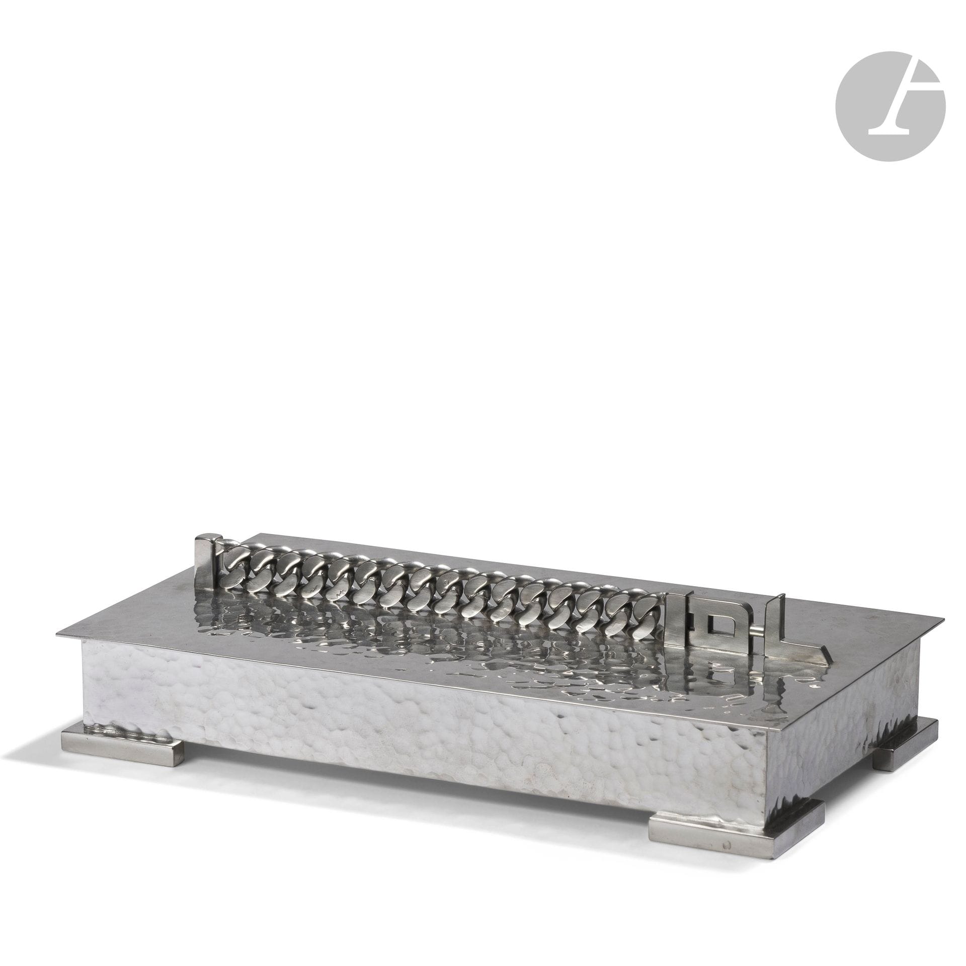 JEAN DESPRÉS (1889-1980)
Rare et important coffret moderniste en argent. La base rectangulaire traitée en martelage repose sur quatre patins d’angle à surface lisse. Le couvercle à surface martelée reçoit la prise formée d’une gourmette et d’un monogramme. Porte le poinçon de Maître Orfèvre sur le couvercle et celui de garantie à trois reprises (deux fois sur les patins et une fois sur le couvercle). H.5,5cm – L.23,5cm – L.13,5cm – Poids:1512,9 g