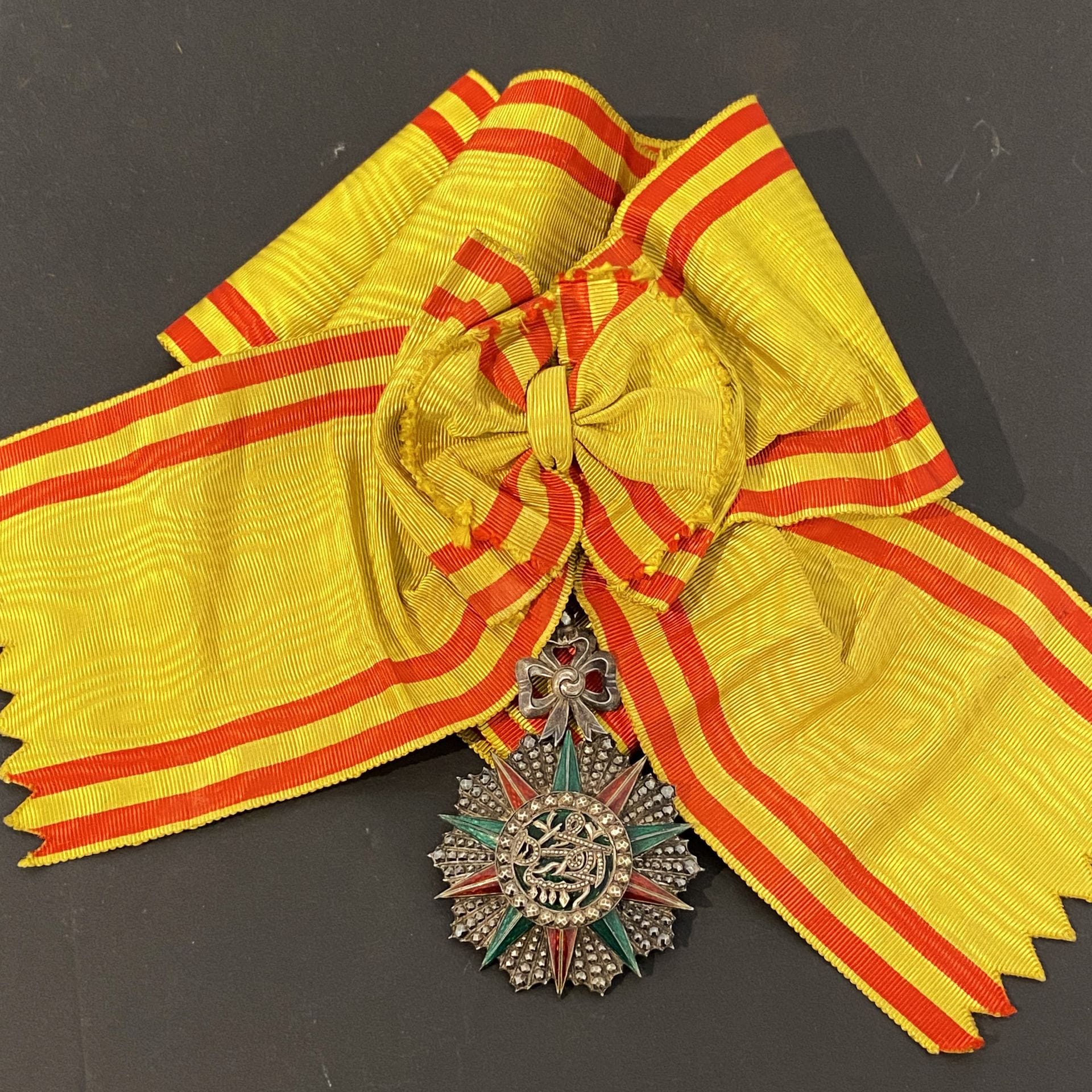TUNISIE 
ORDRE DU NICHAN IFTIKHAR
Bijou de grand-croix au monogramme de Mohammed El HABIB (1922-1929). 
En argent ciselé et travaillé à pointes de diamant. Le centre à fond émaillé vert. 
Poinçon tête de sanglier et d’orfèvre. Revers uni avec marque « BIJOUTERIE ORDRES MÉDAILLES LEMAITRE 346 St HONORE PARIS » 
86 x 60 mm - Poids brut : 58 g
Avec son écharpe à nœud. 
T.T.B. (Petit cheveu).