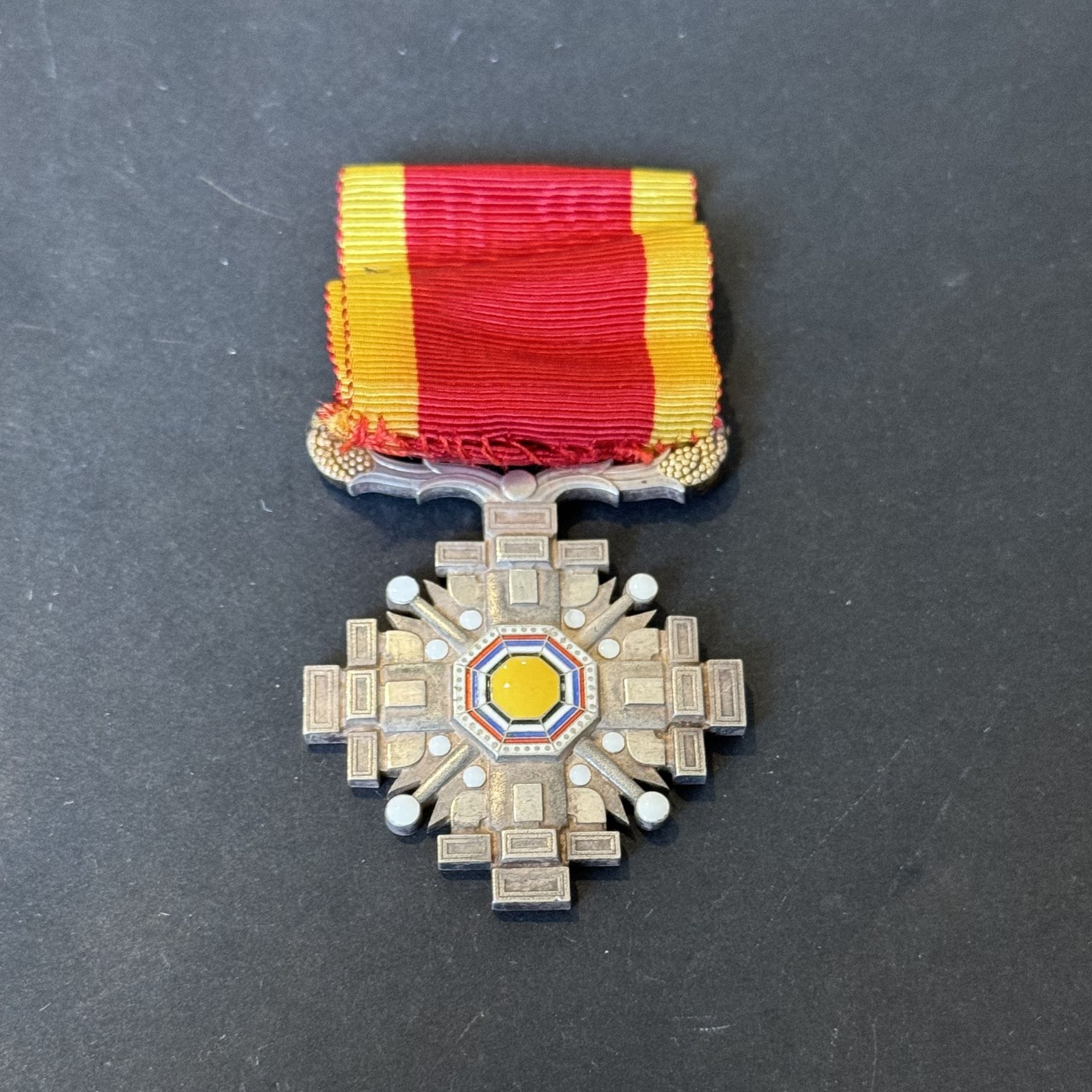 CHINE (MANCHUKUO)
ORDRE DES PILIERS DE L’ÉTAT 
Insigne de chevalier en métal argenté et émaillé.
Ruban. Dans une boîte de l’ordre du Trésor sacré. 
51 x 40 mm
T.T.B. à SUP.