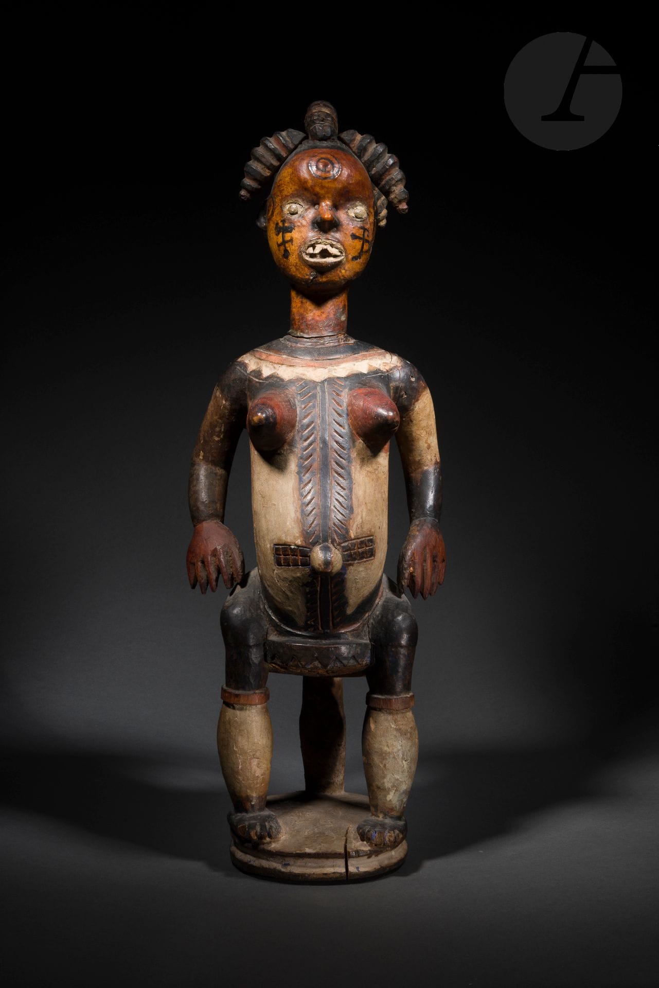 Une rarissime et importante représentation de femme assise sur un tabouret, la tête à la présence intense est recouverte de cuir d’antilope, sa coiffe est constituée de multiples tresses, sculptées indépendamment, et rapportées. Son corps est orné des représentations de scarifications rituelles gravées mais aussi d’un beau décor d’une polychromie ancienne. On connaît les très nombreuses sculptures de tête-cimier du peuple Ejagham (appelé Ekoï par les Efik), sculptures recouvertes de cuir, qui constituaient d’ailleurs une contribution unique dans l’histoire de l’art, mais quasiment aucune statue en bois de ce type avec la tête recouverte de cuir d’antilope. La tradition de cimiers recouvert de cuir est partagée par bien d’autres groupes mais la paternité de l’invention de ces créations en revient au peulpe Ejagham. Cette sculpture rare avait d’ailleurs été choisie par Marie Louise Bastin pour illustrer son chapitre sur les Ekoï dans son ouvrage Introduction aux Arts d’Afrique Noire, qui reste jusqu’à aujourd’hui un des grands ouvrages de référence sur les arts d’Afrique. Il faut absolument noter un détail important qui contribue à l’extrême rareté et l’importance de cette oeuvre: la présence sur le visage (en plus des scarifications en cercles concentriques) de tatouages représentant des idéogrammes nsibidi, qui constituait une ancienne écriture utilisée dans des circonstances sacrées et profanes, et qui survit dans le rituel d’initiation et des funérailles des membres importants de la société Ngbe. 
Ejagham (Ekoï), Nigeria
Bois, clous, cuir et pigments rouge, blanc, noir et bleu, fentes et usures d’ancienneté, très belle et ancienne patine d’usage.
H.: 72cm

Provenance:
Collection Antonio Segui, Paris
Transmis par descendance

Publication:
Bastin, Introduction aux Arts de l’Afrique noire, 1984, p.231, n°235