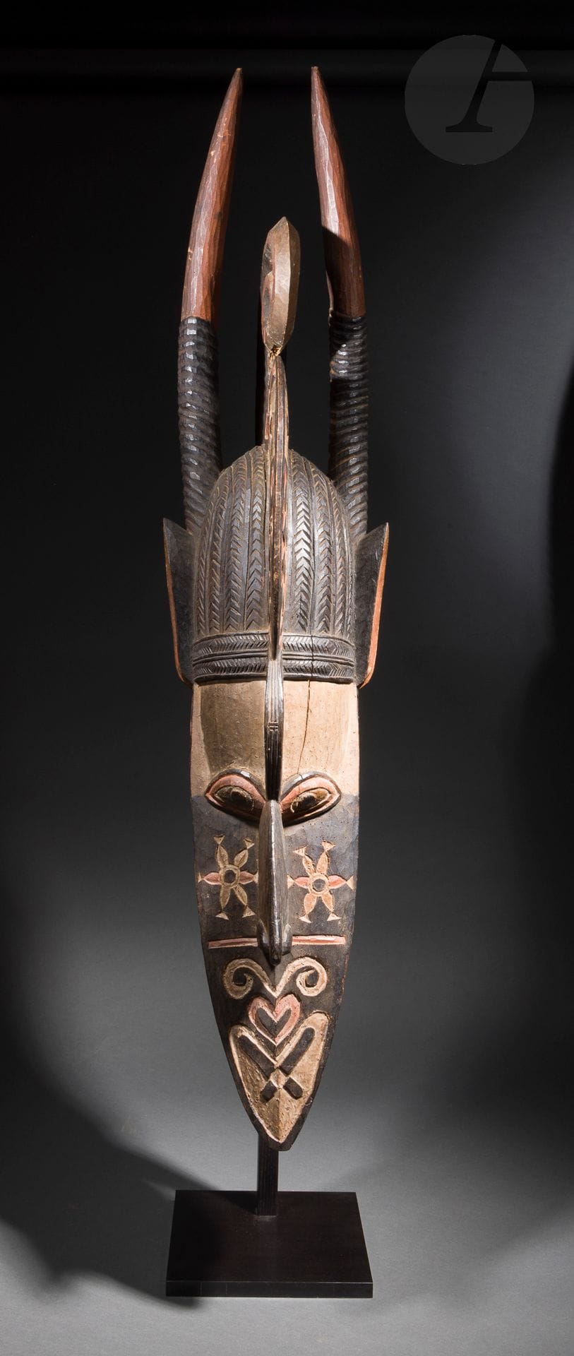Un ancien et grand masque banda, grand classique de l’art des Baga et des Nalu de la côte de Guinée, masque emblématique et représentation faisant fusionner l’homme à des animaux terrestres et marins, formé d’un enchevêtrement de motifs ici particulièrement réussi. La longue mâchoire du crocodile est ouverte, les yeux et le nez saillants. Il porte la haute coiffure élaborée des femmes Baga et Nalu dont les tresses sont représentées par des lignes en chevrons gravées. Il se termine par une composition formée de deux oreilles animales et deux longues cornes d’antilope. Le très beau décor polychrome d’un style bien ancien - noir, rouge et traces de kaolin- se distingue par son traitement en motifs gravés et non en aplats peints comme le sont généralement les masques plus modernes. Autrefois considérés comme sacrés, les masques banda interviennent aujourd’hui lors de fêtes de divertissement et sont visibles par tous (F. Lamp, Art of the Baga, 1996, p.146).
Baga/Nalu, Guinée
Bois, pigments ancien, usures et petits manques (casses anciennes), très belle oxydation. d’ancienneté.
H.: 136cm

Provenance:
Collection privée, Paris
