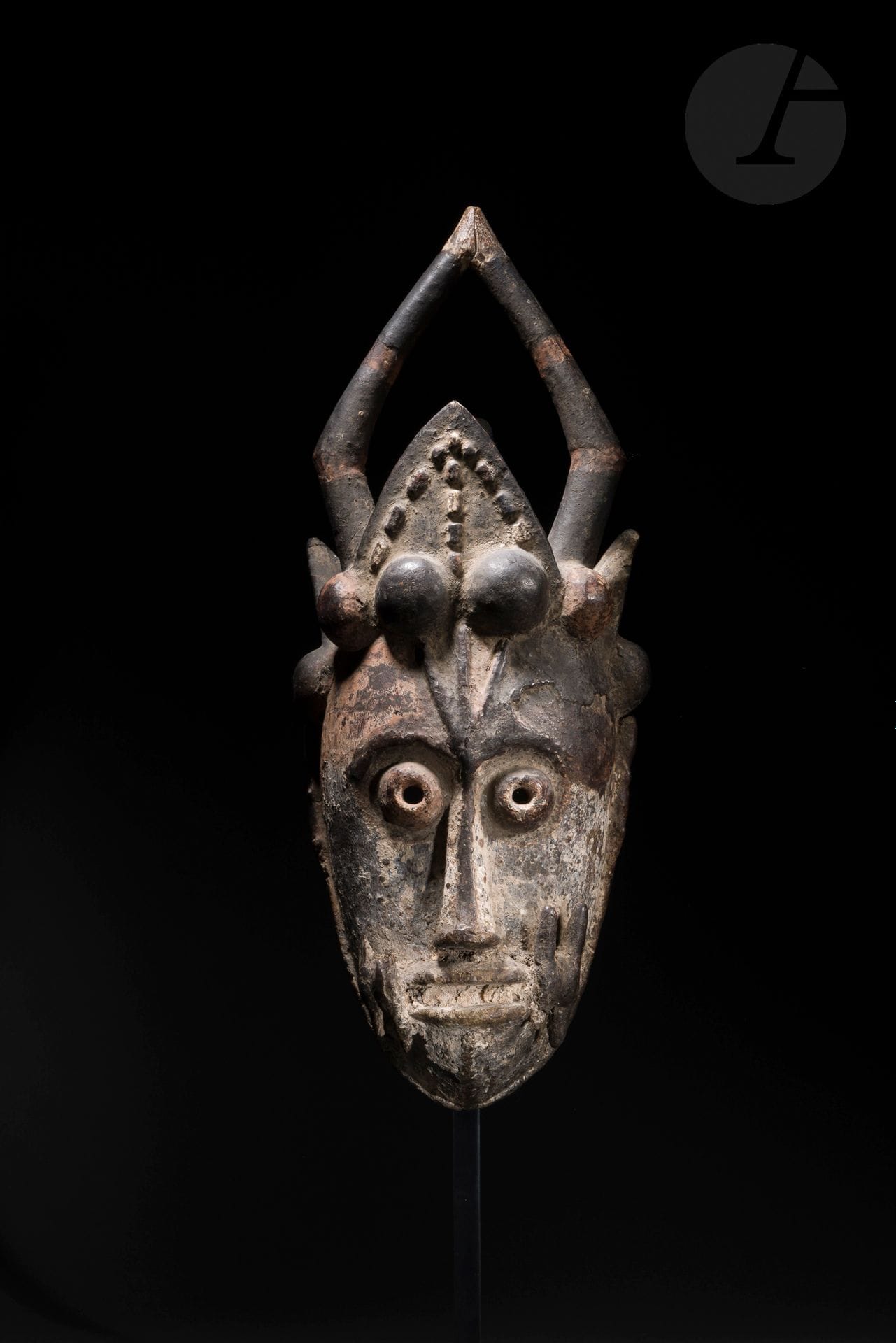 Un très ancien masque de danse oniedjo d’une typologie rare, orné d’un personnage sculpté au sommet à l’arrière de la coiffe et regardant à l’opposé du masque, probable attribut de protection, ainsi que de deux reptiles en relief sur les flancs et d’ornements de part et d’autre de la bouche. Les contrastes de sa polychromie (rouge, blanc et noir) accentuent la présence hypnotique de ses yeux sculptés en forme de perles. 
Urhobo, Nigeria
Bois, pigments, accidents et casses anciennes visibles, très belle et épaisse patine sacrificielle et d’usage. 
H.: 50cm

Provenance: 
Collection Yves et Ewa Develon, Paris
Collection Hélène Leloup, Paris, acquis en 1985
Transmis par descendance

Publication:
Arts d’Afrique noire, n°58