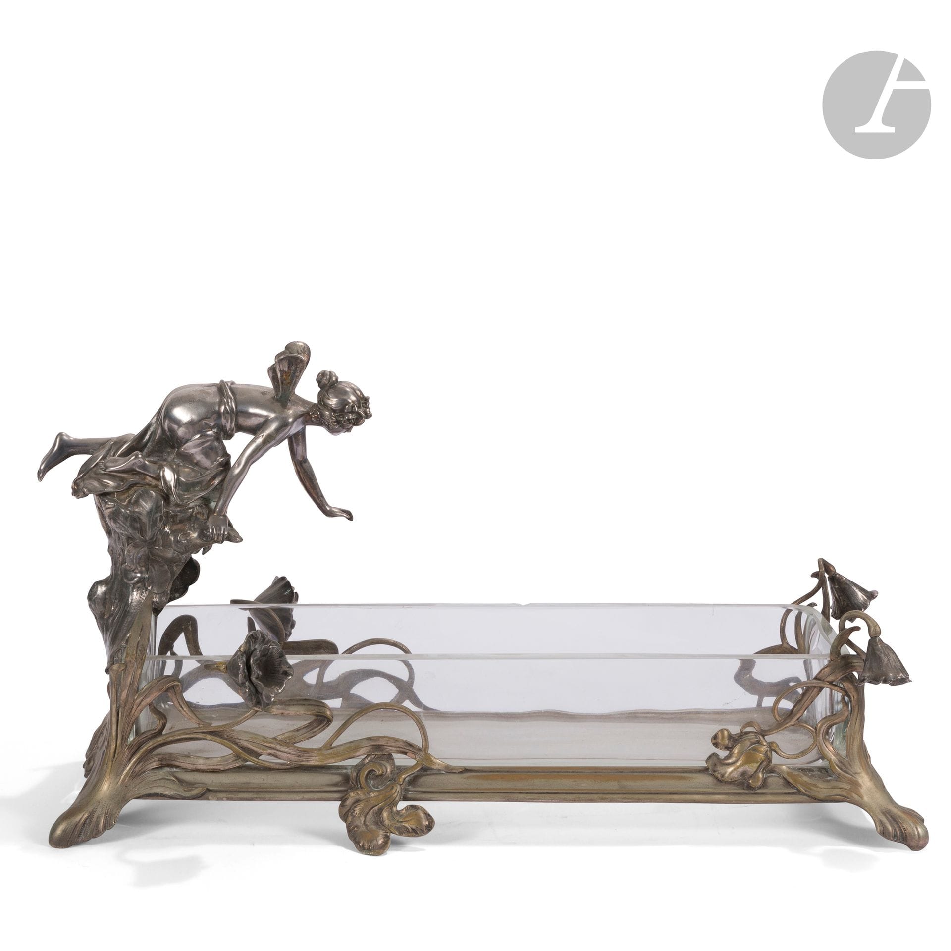 WMF – WÜRTTEMBERGISCHE METALLWARENFABRIK
Femme-papillon au-dessus d’un bassin 
Très importante jardinière formant centre de table. La monture en métal et étain argentés. Complet de son intérieur en verre. Époque Art nouveau. Deux éclats en bordure de la partie en verre. Usures à l’argenture. Marquée du cachet WMF au revers.  H. 30 cm – L. 57 cm – l. 23 cm