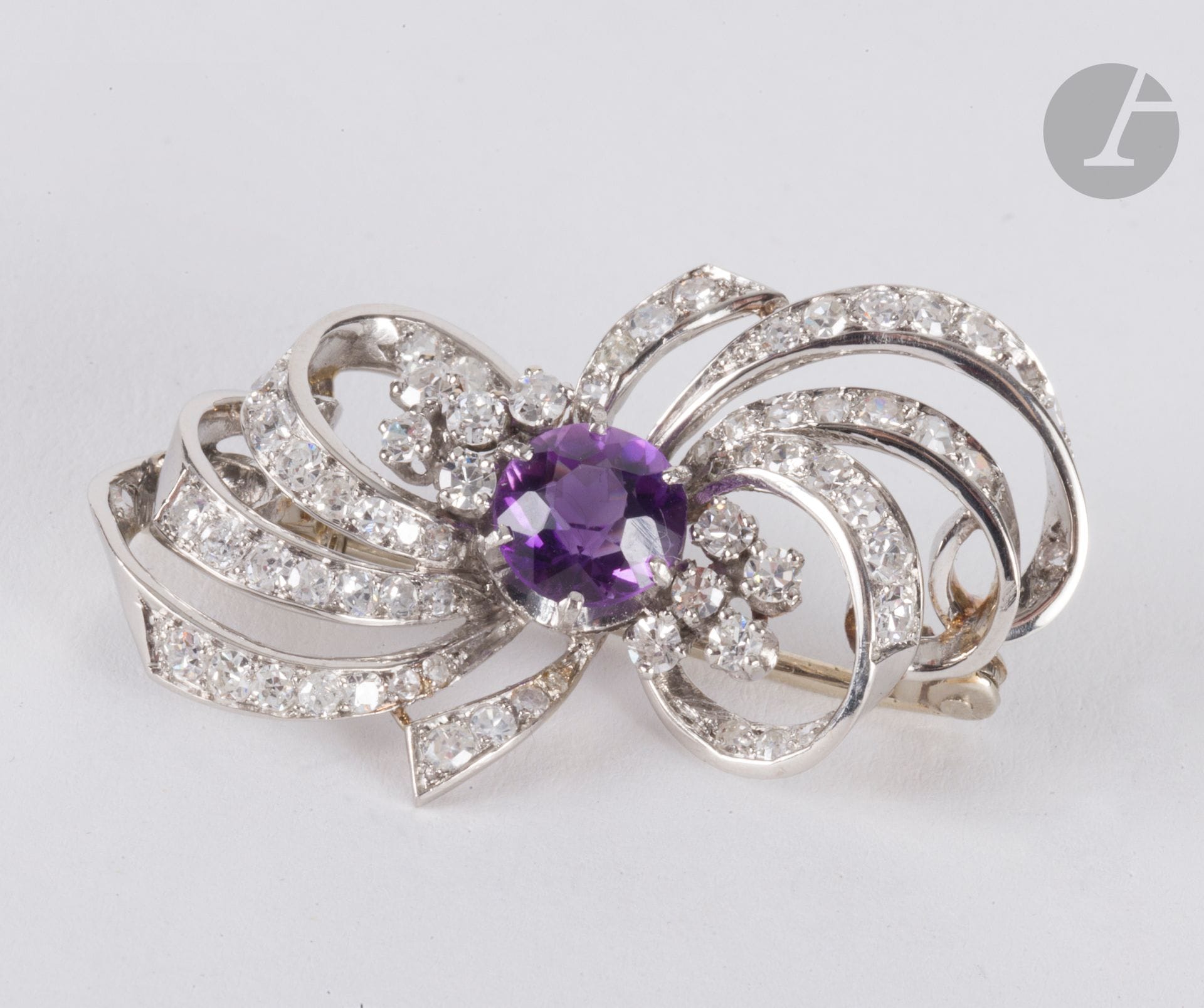 Broche rubans noués en or gris 18K (750), sertie d'une améthyste ronde et de diamants ronds 8/8. Longueur : 3,5 cm environ. Poids brut : 9,3 g (manque, égrisures)