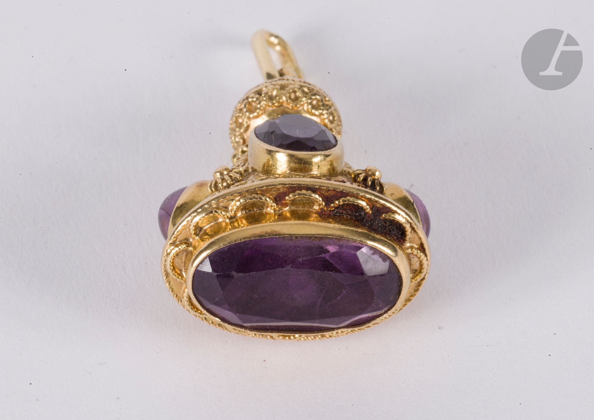 Pendentif breloque en or 18K (750), orné d'améthystes ovales et de motifs en grénetis. Hauteur : 3,4 cm environ. Poids brut : 13 g (choc avec manque de matière)