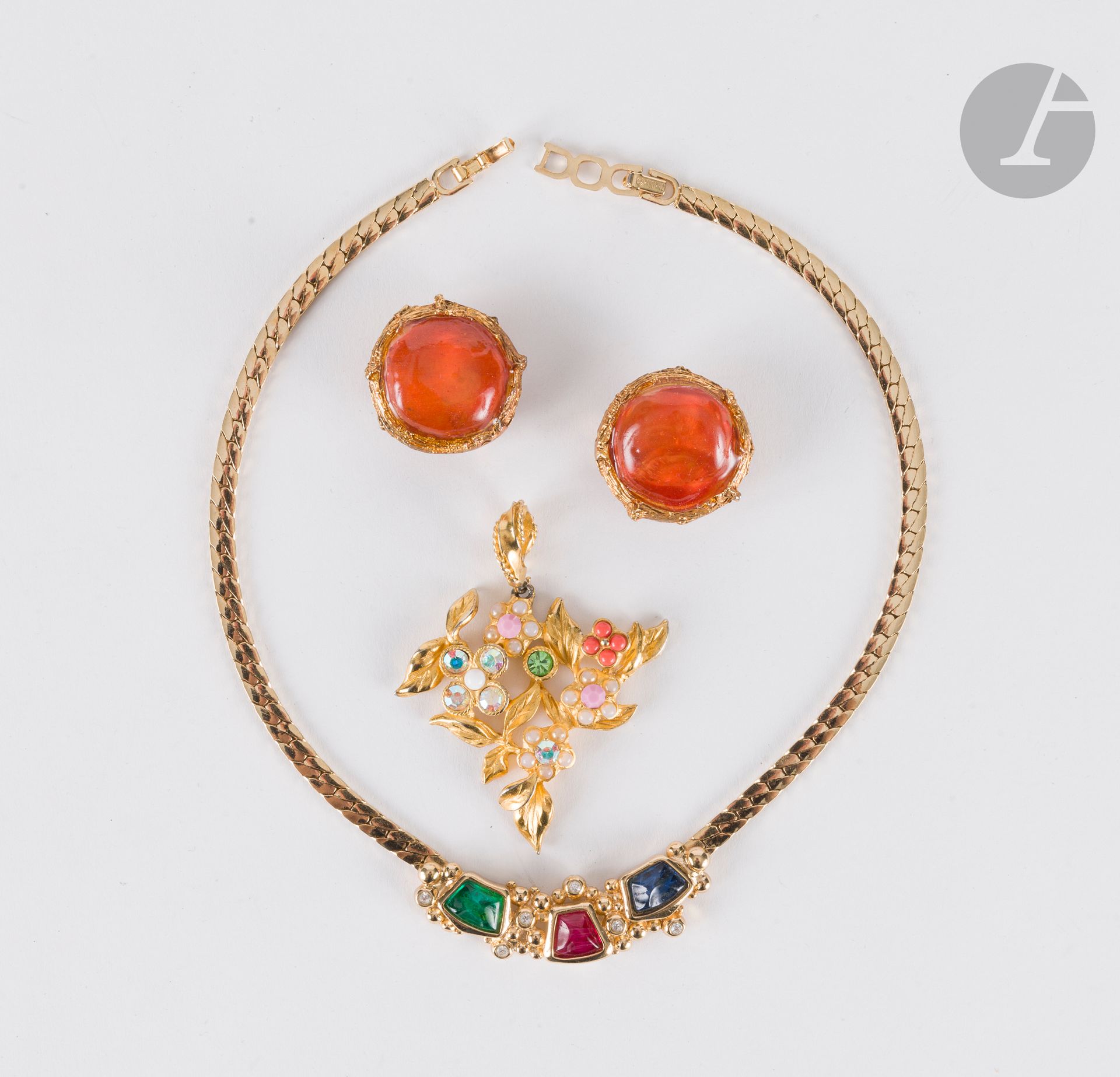 Lot de 3 bijoux fantaisie signés : un collier Christian DIOR en métal doré à décor de trois pierres, verte, rouge et bleue, 39 cm, un pendentif fleurs Christian LACROIX en métal doré, strass et pierres de couleur, 5,5 x 5 cm, une paire de clips d'oreilles métal doré et résine orange L'OR DU SOIR, diam. : 3 cm
