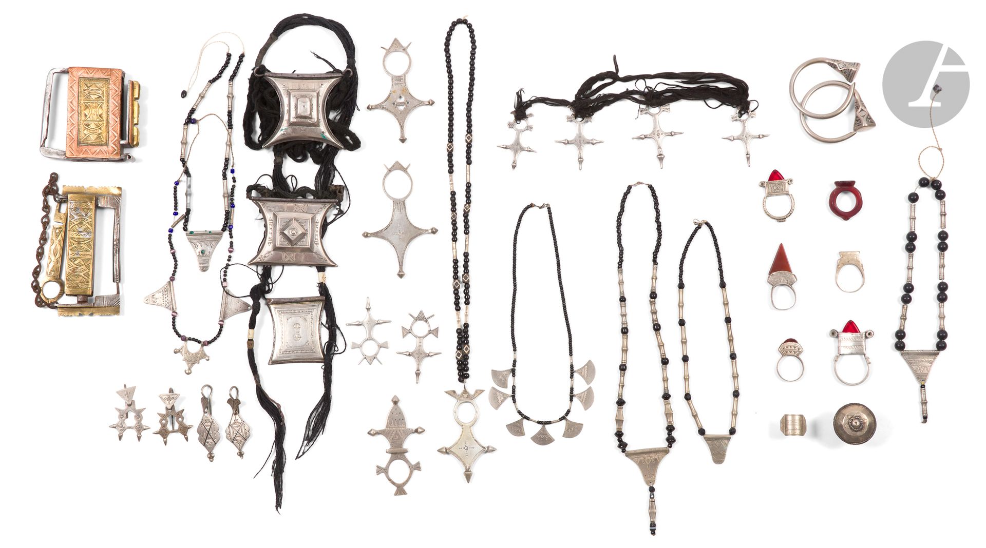 Fort lot de bijoux touareg, Afrique Subsaharienne, XXe siècle 
Trois colliers, enfilades de petites perles noires et perles en argent très bas-titre, des plaques d'argent très bas-titre à décor géométrique gravé en pendeloques, PB : 70 g ; deux colliers à pendentifs Croix du Sud en argent, l'un à un pendentif sur une enfilade de perles noires et d'argent, l'autre à quatre pendentifs sur des liens de laine noire, PB : 79 g ; quatre Croix du Sud en argent, Poids : 47 g ; une Croix du Sud en argent bas titre, Poids : 30 g ; six colliers composés de plaques en métal à décor géométrique gravé sur des enfilades de perles noires et colorées ou sur des liens textiles ; deux pendants d'oreille annulaires en métal et deux paires de pendants d'oreille en argent bas-titre, P. 27 g à décor géométrique gravé ; sept bagues en métal, certaines avec un cabochon de cornaline ou de verre ; une bague en verre rouge. On joint deux cadenas touareg tunast, en fer à garnitures de laiton et de cuivre sur l'un, à décor incisé de motifs géométriques, avec une clef. 5,4 x 10,5 cm et 7,8 x 7,4 cm.