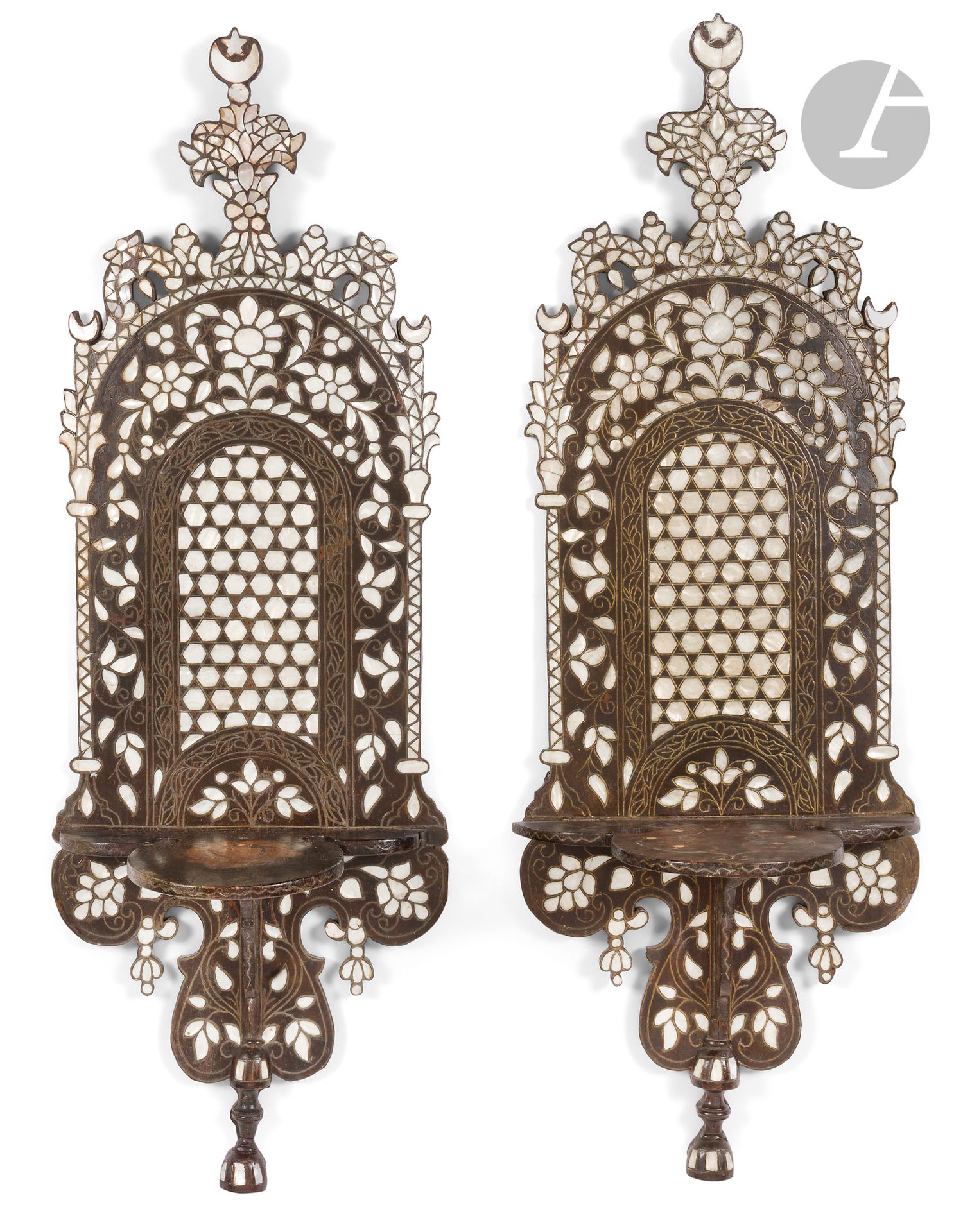 Paire de porte-turbans kavukluk, Syrie, début XXe siècle 
Porte-turbans à découpe chantournée, couronnés d'un petit fronton fleuronné surmonté d'un croissant de lune embrassant une étoile et flanqués de deux colonnettes surmontées d'un croissant de lune. En bois à décor incrusté de fils métalliques et de plaquettes de nacre dessinant un panneau géométrique comblant une niche entourée d'une frise florale. Une des deux tablettes incrustée de fils métalliques.  
94,9 x 32,5 cm et 94,5 x 32 cm 
Sauts de vernis, usure, petits manques, petites restaurations, un clou manquant en partie basse, trace plus claire sur une des deux tablettes, anneaux de suspension fixés au dos. 

Provenance : Collection Maison Tarazi.
