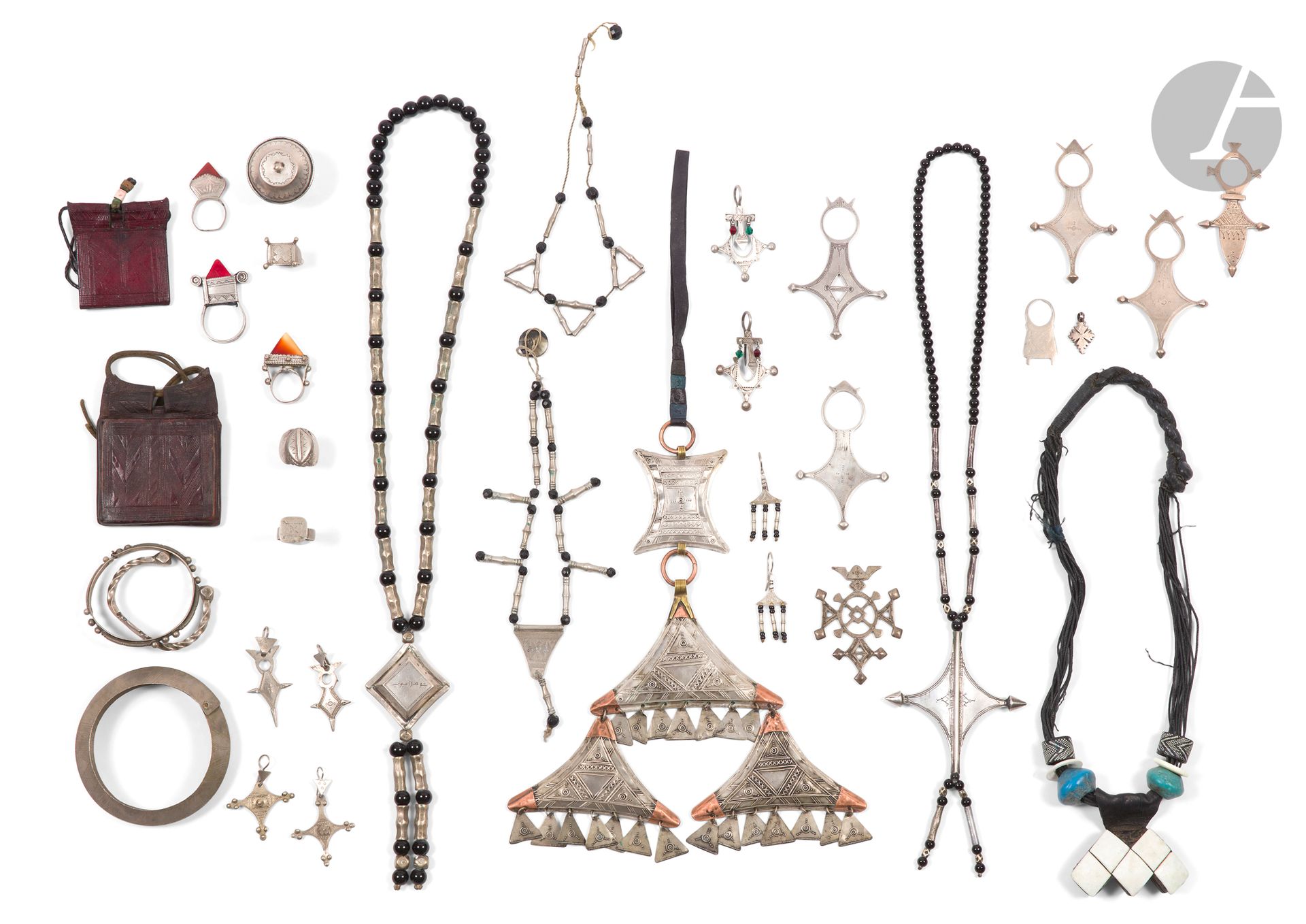 Fort lot de bijoux touareg, Afrique sub-saharienne, XXe siècle 
Deux paires de pendants d'oreilles en argent bas-titre et petites perles de verre, PB. 15 g ; quatre pendants d'oreille pouvant former paire en métal ; sept bagues en métal, certaines avec un cabochon de verre ou de cornaline ; trois colliers en métal et perles noires, le plus grand au pendentif gravé d'un décor géométrique et d'une inscription en arabe ; trois bracelets en métal, l'un torsadé, l'un à décor perlé, un troisième à décor géométrique ciselé ; un grand pendant en métal à garnitures de cuir et laiton composé de quatre plaques à décor géométrique disposées en pyramide, trois évoquant des khamsa ; un collier, enfilade de perles noires avec une Croix du Sud en argent en pendentif et trois Croix du Sud en argent, PB. 106 g ; trois Croix du Sud et deux pendentifs en métal. On joint trois colliers composés de liens de cuir, perles colorées et pendentifs en cuir estampé.  
Quelques accidents et traces d'oxydation, en l'état.