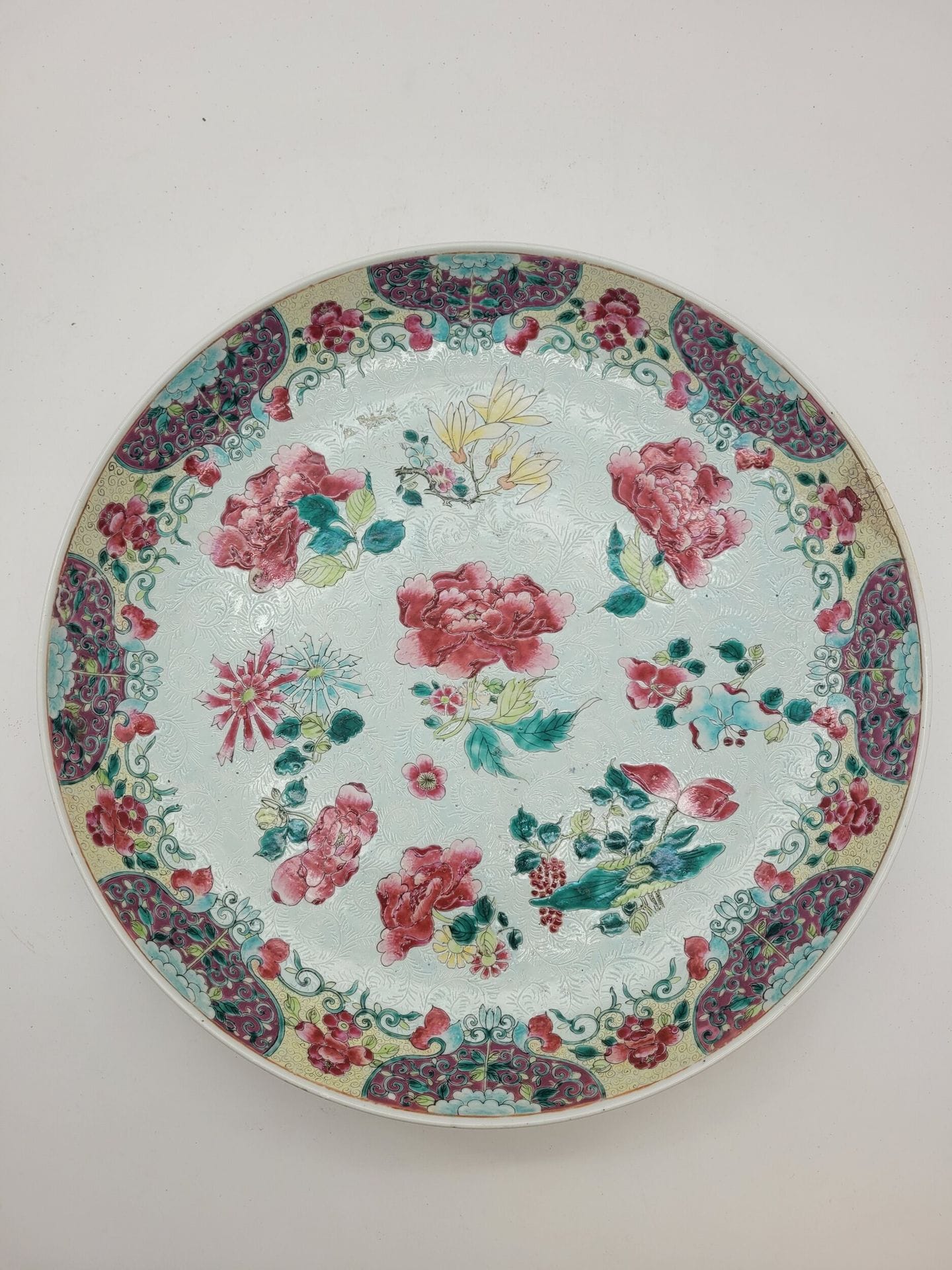 Grand plat en porcelaine dans le style de la famille rose, Chine, XIXe siècle
A décor de divers fleurs sur fond bleu au centre et sur fond jaune sur le marli. Décor de branches fleuries au verso du marli. 
Diamètre : 39,6 cm
Accidents et restaurations.