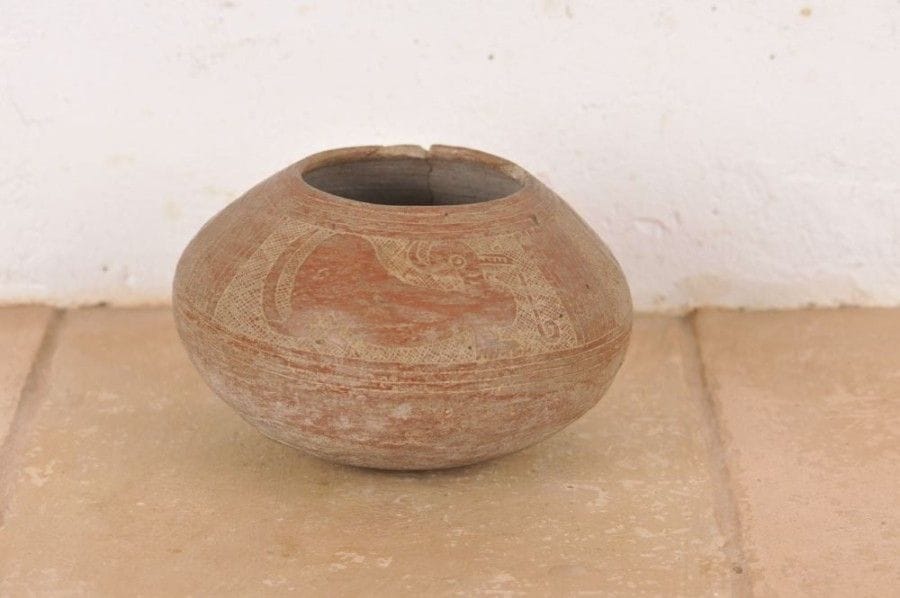 Vase globulaire orné d’une frise de trois félins laissés en réserve sur un fond quadrillé.  Ils sont parés de bracelets et une volute s’échappe de leur gueule. Terre cuite brune à engobe rouge au décor gravé. Traces de brûlure. Culture Cuasmal, Équateur, 800 - 1500 ap. J.-C. H : 10 cm - Diam : 15 cm État : cassé et recollé. Petits manques sur le col.