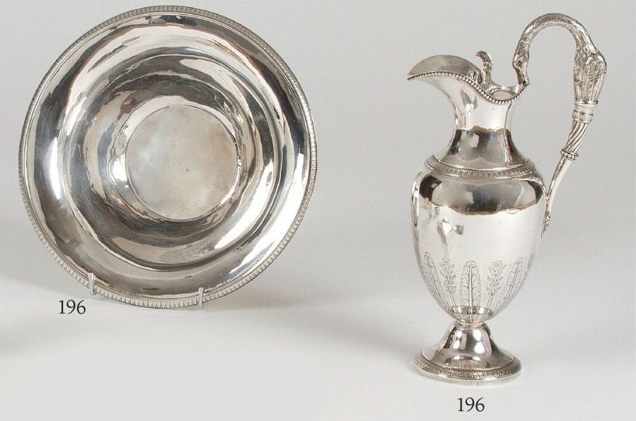 Aiguière et son bassin de forme ronde en argent.L’aiguière de forme ovoïde repose sur un piédouche bordé d’un décor à la molette à feuilles de laurier en rappel sur son bassin. Le corps est ciselé d’un décor de larges feuilles et le bec bordé d’un rang de perles. L’anse figure un cygne fixée au corps par une tête de Mercure ceint dans un médaillon. Le bassin présente des restaurations et des traces de soudure.Province 1819 - 1838.Poinçon d’orfèvre indéterminé : FLL. Poids : 1407 gH. : 33,2 cm - D. du bassin : 30 cm