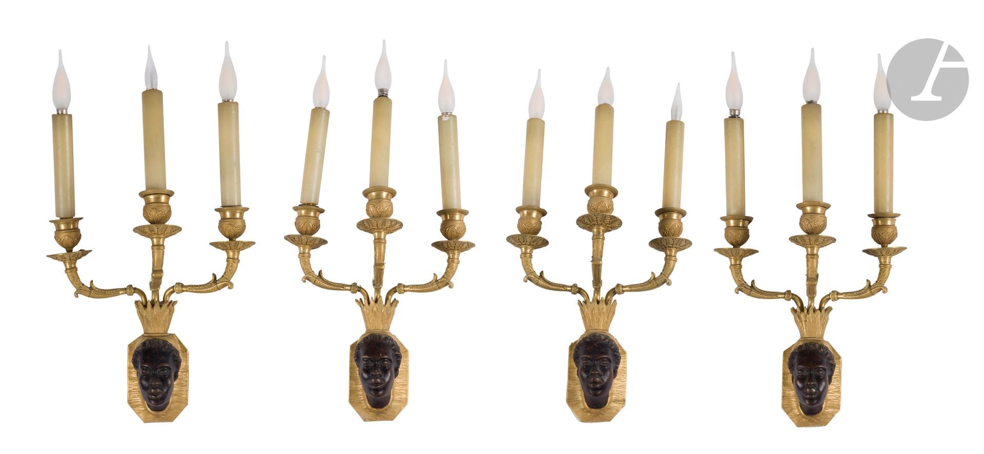 Suite de quatre appliques aux nubiens en bronze patiné et doré, à trois bras de lumière et décor feuillagé; (montées à l’électricité).
XIXe siècle.
H.: 28cm, L.: 23cm