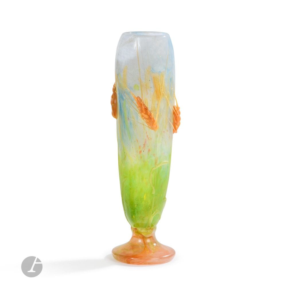 DAUM FRÈRES – VERRERIES ARTISTIQUES DE NANCY
Les Blés sauvages - Hommage à Claude Monet, vers1905, seul exemplaire de ce modèle connu à ce jour, verrerie artistique probablement réalisée à l’époque pour une exposition
Exceptionnel vase en obus fuselé reposant sur piédouche.
Épreuve en verre multicouche; le décor titre tournant figuré par des épis barbus rendus par d’importantes applications en verre teinté orange dans la masse modelées et collées à chaud sur un fond traité dans le goût d’un tableau impressionniste, simulant un champ herbeux laissant apparaître de possibles coquelicots et exécuté en colorations intercalaires – la partie haute évoquant un ciel clair.
La base du corps du vase reçoit également des applications formant les tiges et les feuilles de l’orge.
Le piédouche aux colorations marmoréennes en nuées.
Quelques cheveux de la barbe des épis interrompus à l’origine.
Signé DAUM Nancy à la Croix de Lorraine, en intaille vers la base du corps du vase.
Hauteur: 33,5cm

Archives et œuvre en rapport:
Musée d’Orsay, Paris – Une variante de notre œuvre, avec un papillon en application, reproduite et référencée dans le dossier documentaire consacré à la maison Daum Nancy, conservé à la documentation de la conservation de cette institution. 

Bibliographie et œuvre en rapport:
Noël Daum – Daum maîtres verriers – Éditions Édita/Denoël, Lausanne, 1980. Une variante de notre œuvre, avec un papillon en application, reproduite page 79.