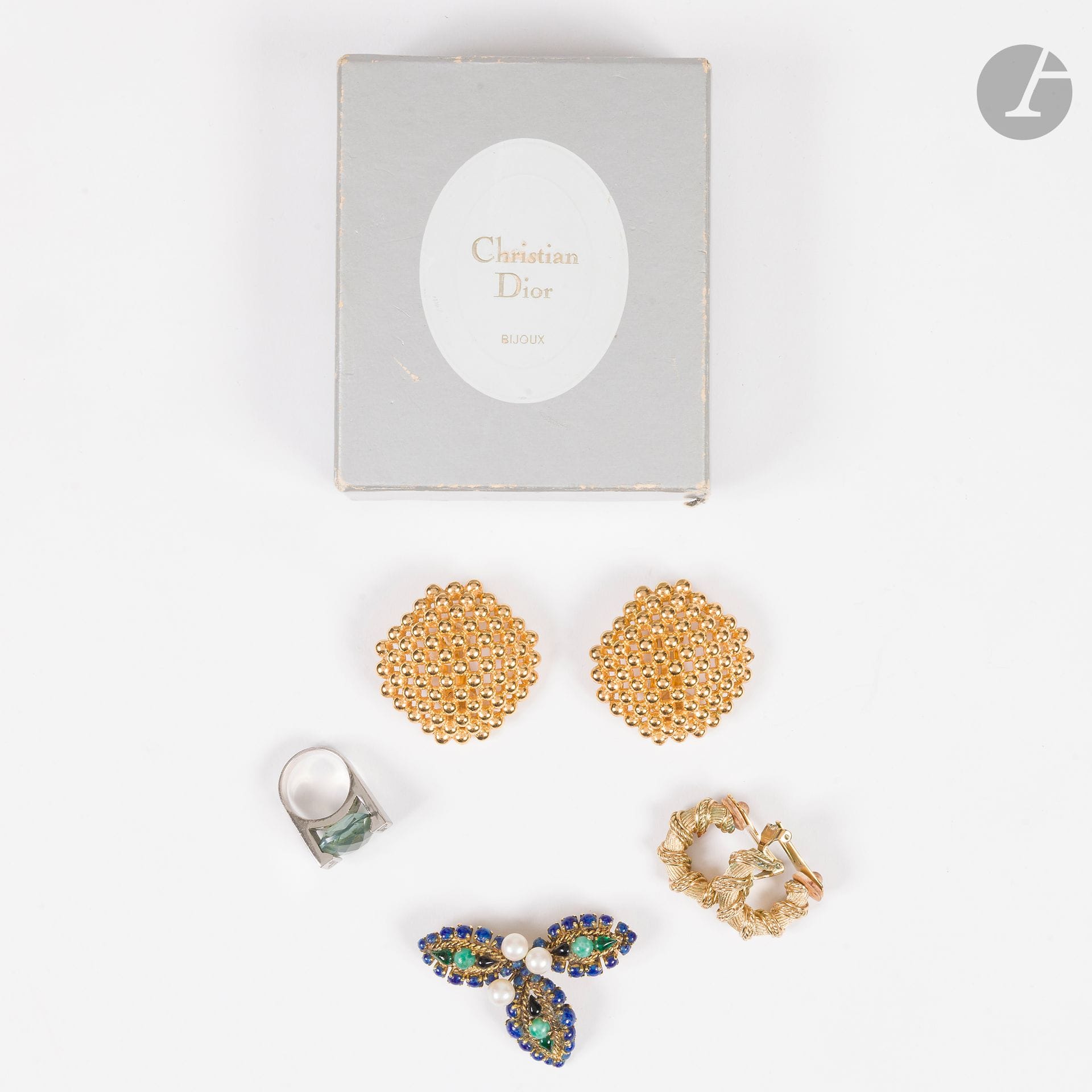 CHRISTIAN DIOR
Lot de quatre bijoux fantaisie. Signés. Dans une boîte de la maison :
- une paire de clips d'oreilles créoles torsadées en métal doré. 2,5 cm
- une paire  de clips d'oreilles losange formé de petites billes. 4,5 cm
- une broche à trois feuilles en métal doré, petites perles et pierres de couleurs. 6 cm
- une bague en métal argenté sertie d'une grosse pierre vert d'eau facetée. T.54 indiquée