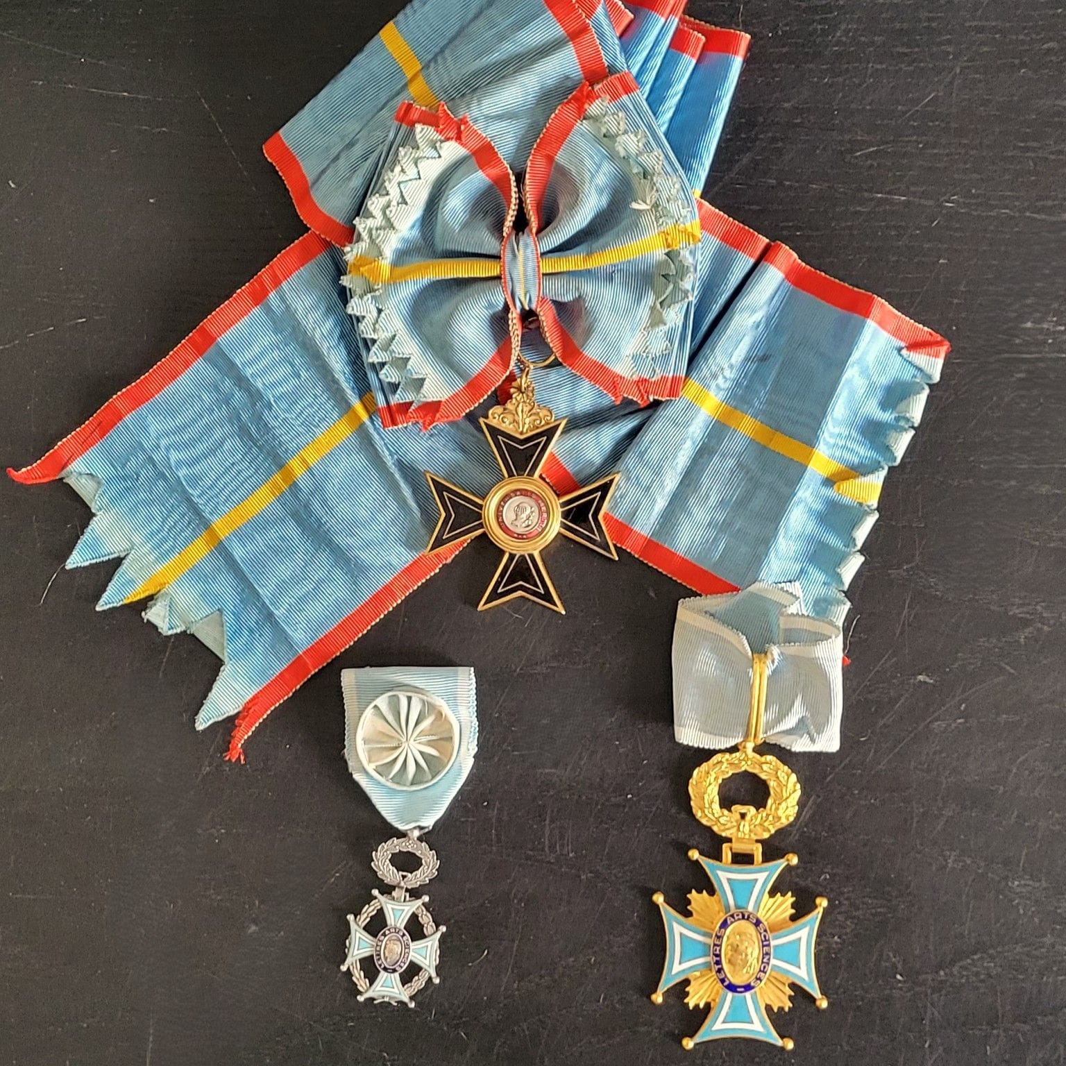 ORDRES DE FANTAISIE 
- Ordre du mérite universel. Bijou de grand-croix. Bronze doré et émail (cheveux). Écharpe avec nœud. 68 x 55 mm 
- Ordre de la société académiques des arts-sciences et lettres. 
Deux pièces : une croix de commandeur et une croix d'officier. Bronze doré, bronze argenté et émail. Cravate et ruban à rosette. 
T.T.B