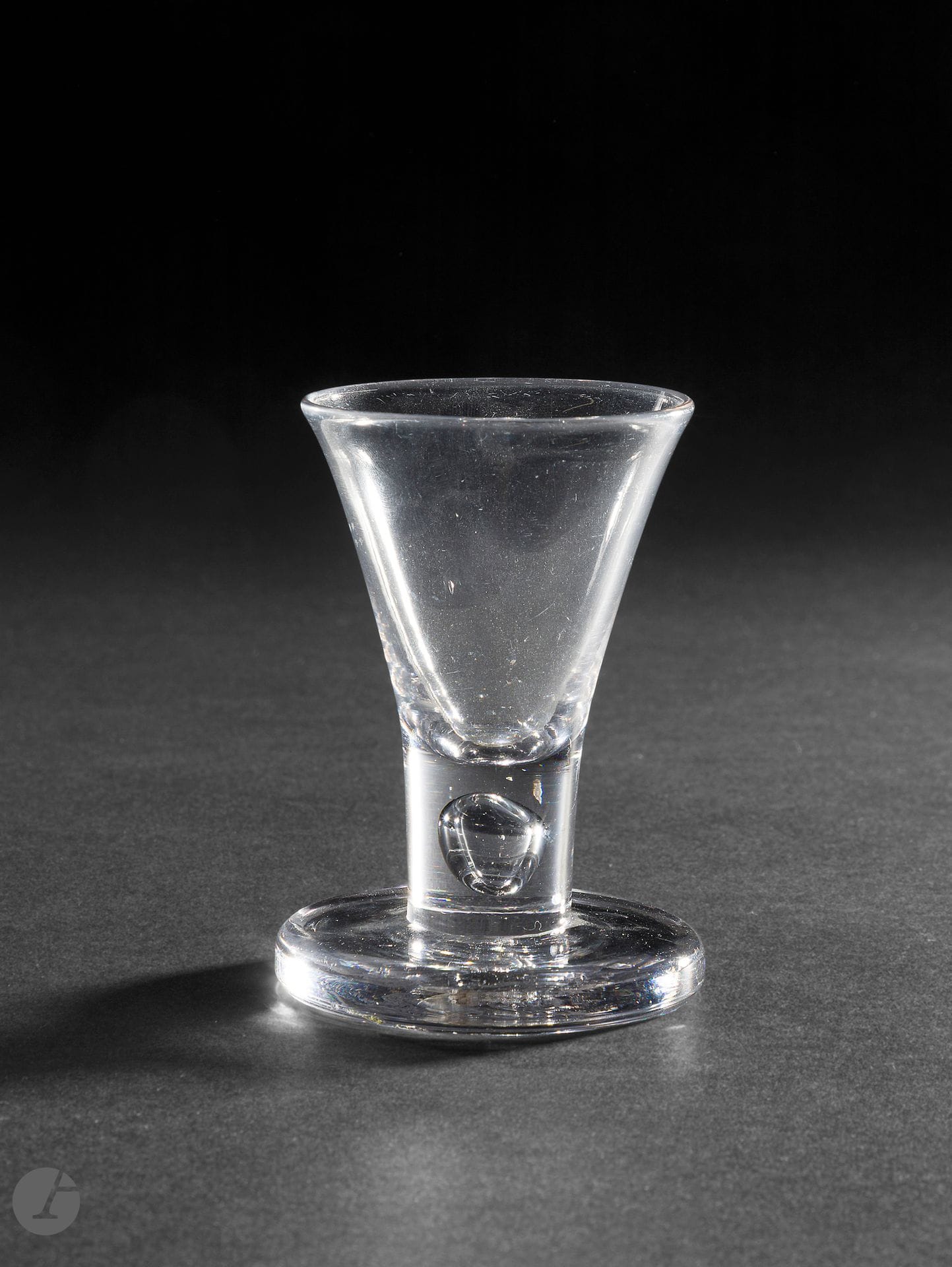 A crystal tap glass or firing glass. The leg features a rounded teardrop. 
England, circa 1750.  
H. 9 cm

The thick stems of these glasses were used to tap the table to attract attention or to ask to speak at English club meetings. 
(See also Lauenstein glassware).

Provenance :
Namara Fine Art 1998
