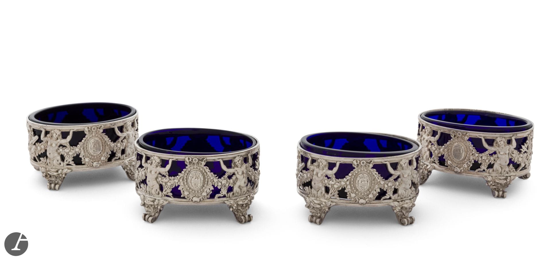 PARIS 1779 - 1780
Set of four oval salt cellars in chased cast silver, complete with blue glass. Four scrolled feet seem to serve as pedestals for the body, decorated with two mermaids on either side framing an enrubanné medallion engraved with a coat of arms. 
Master silversmith: François-Alexis CARRON, received in 1777
Net weight: 398 g