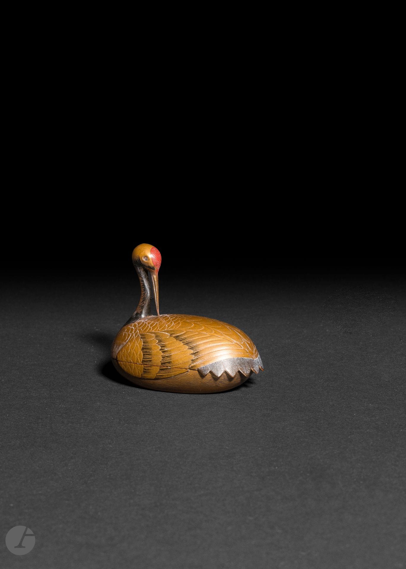 Petit kogo en bois laqué en forme de tsuru (grue à tête rouge) allongée, la tête tournée vers l'arrière, le bec pointé vers son dos. Il est en laque or et noir tandis que le sommet de la tête est laqué rouge. Les ailes traitées en hiramaki e et takamaki e or. La tête et le haut du corps font office de couvercle tandis que le bas permet de contenir l'encens. L'intérieur et le fond sont en laque nashiji. 
Japon, époque Edo, XIXe siècle.
H. : 6,5 cm