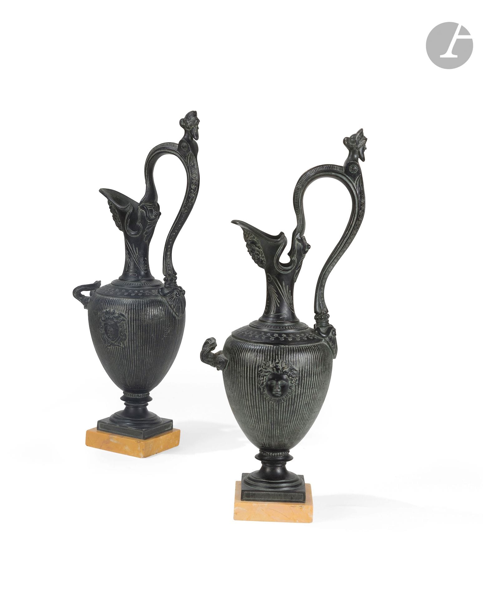 Paire d'aiguières d'ornement en bronze patiné, à décor dans le goût néo-grec de mascarons, buste et palmettes gravées, sur un socle en marbre jaune antique ; (usures).
Vers 1860-1870.
H. : 43 cm