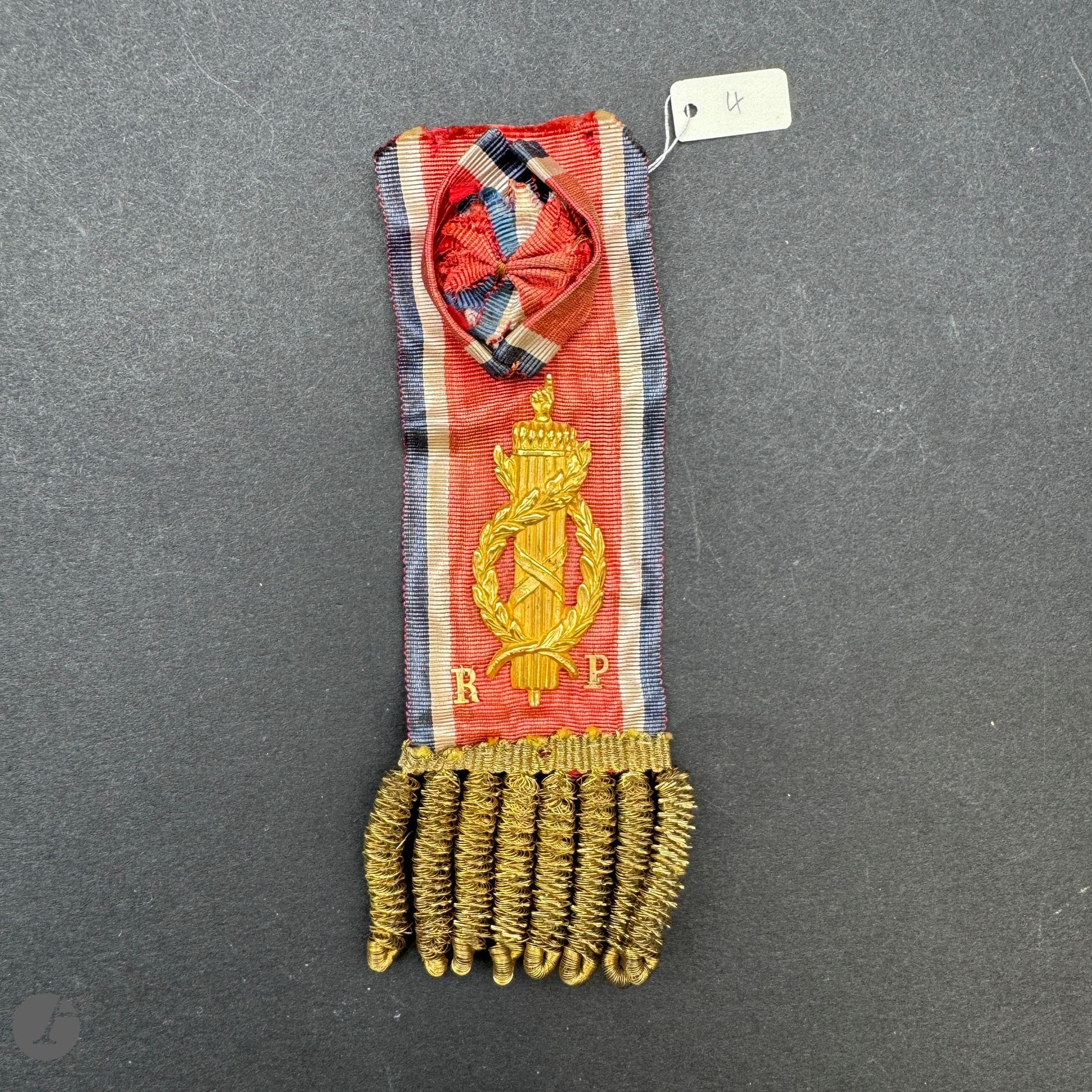 FRANCE 

Insigne de député à l’assemblée constituante (1848-1849).

En moire tricolore, avec rosette ovoïde, bordée dans la partie inférieure de franges en passementerie dorée. 

Motif au faisceau de licteur et lettres « R » et « P » en laiton doré, cousu au ruban. 

Revers avec attache de boutonnière. 

11,5 x 3,5 cm 

B.E.